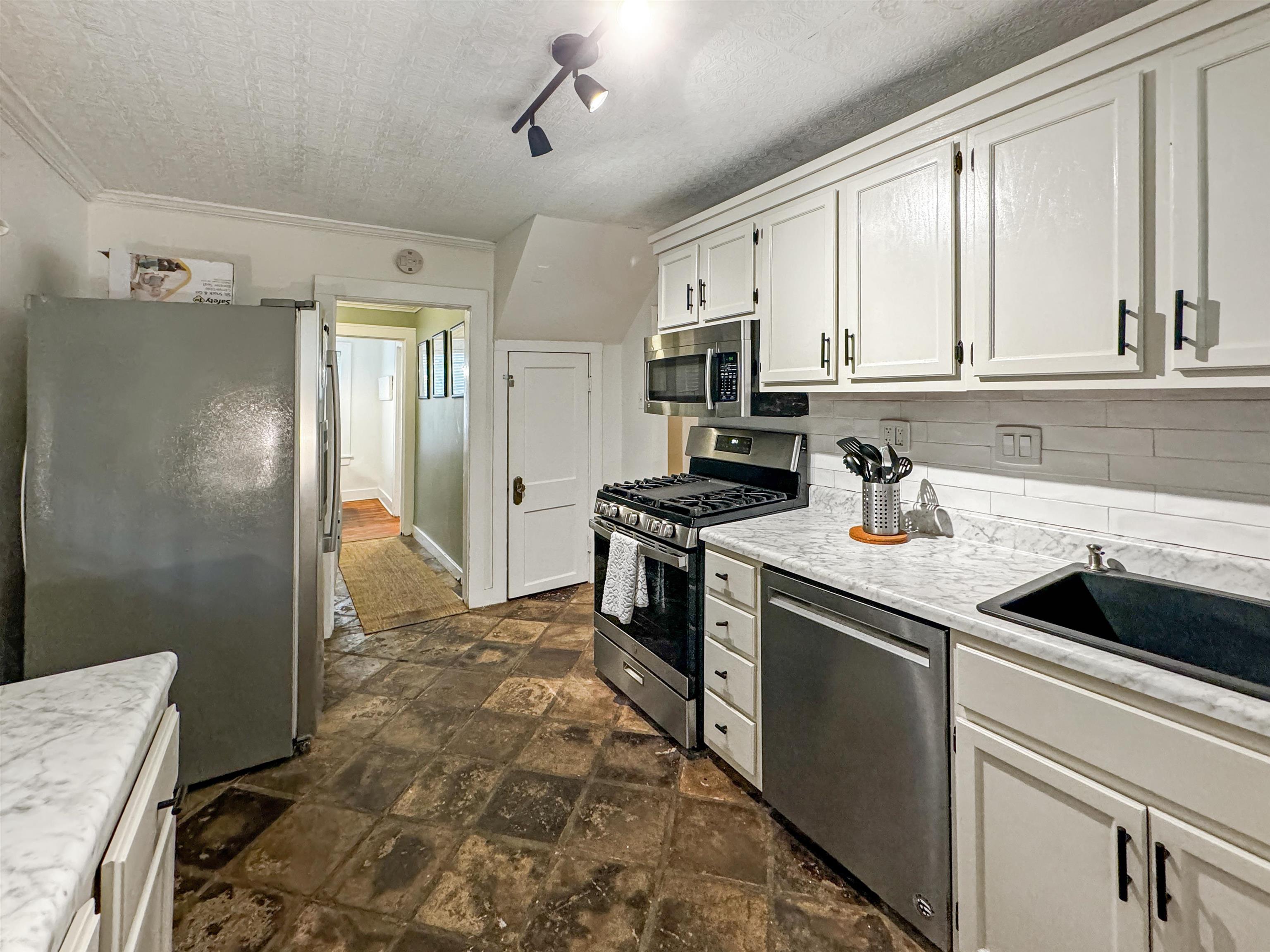 Kitchen with white cabinets, backsplash, appliances with stainless steel finishes, and crown molding