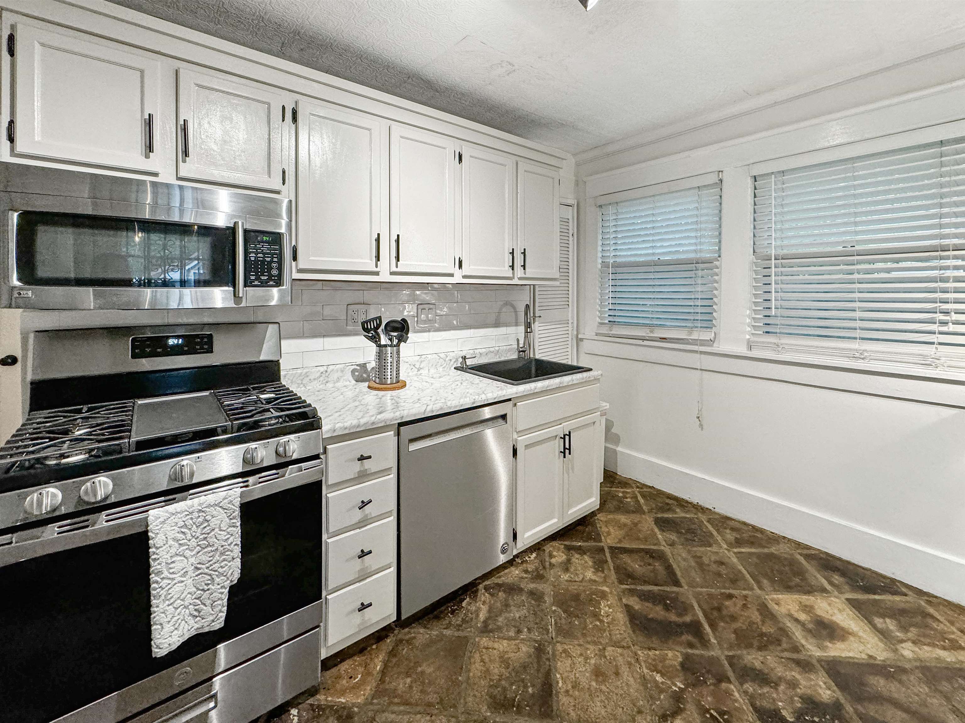 Kitchen featuring appliances with stainless steel finishes, decorative backsplash, sink, and white cabinets