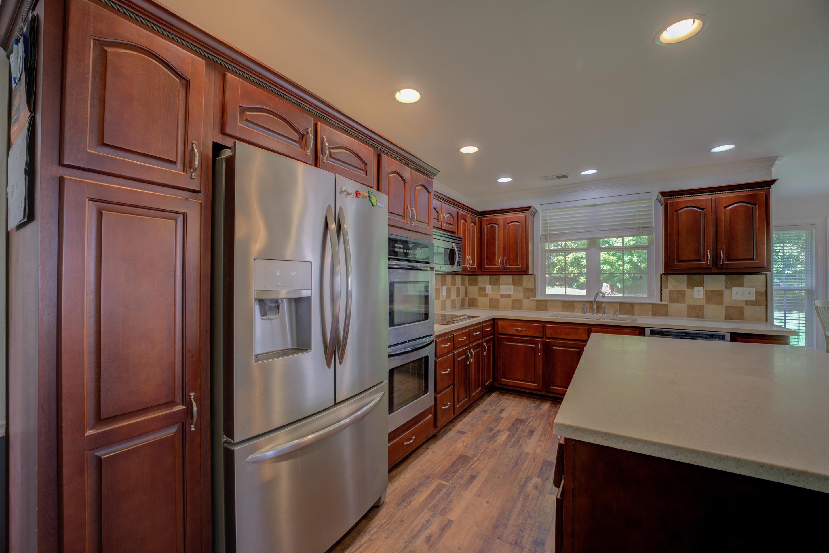 Kitchen with backsplash, hardwood flooring, appliances with stainless steel finishes, and plenty of natural light.