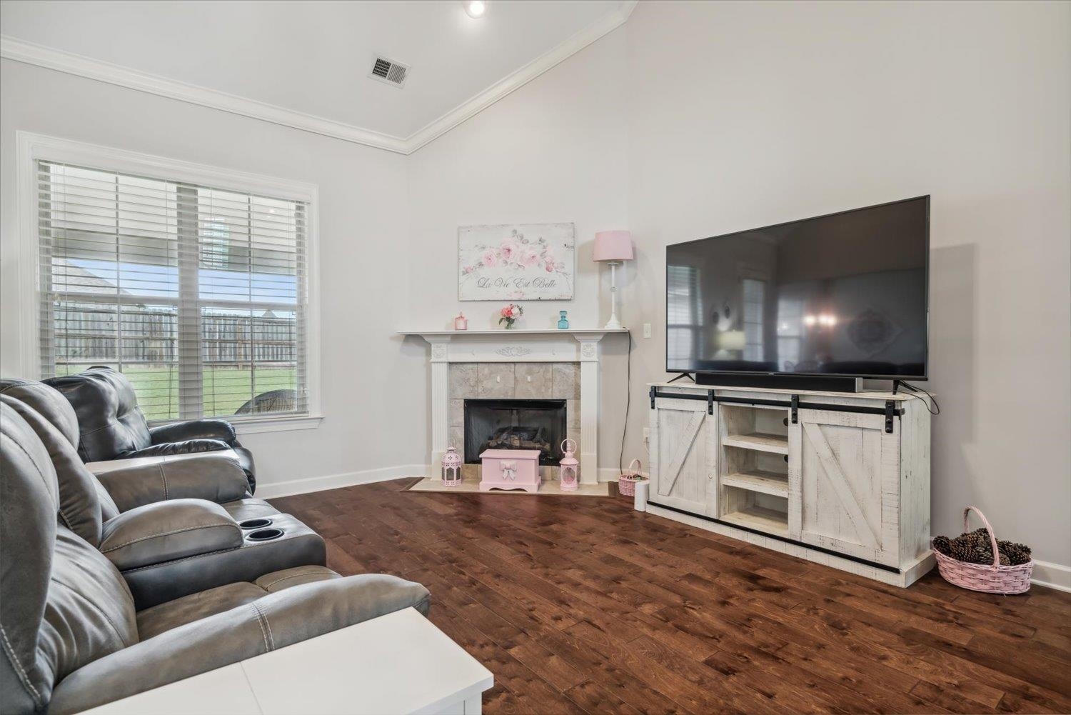 Living room with a fireplace, ornamental molding, dark wood-type flooring, and high vaulted ceiling