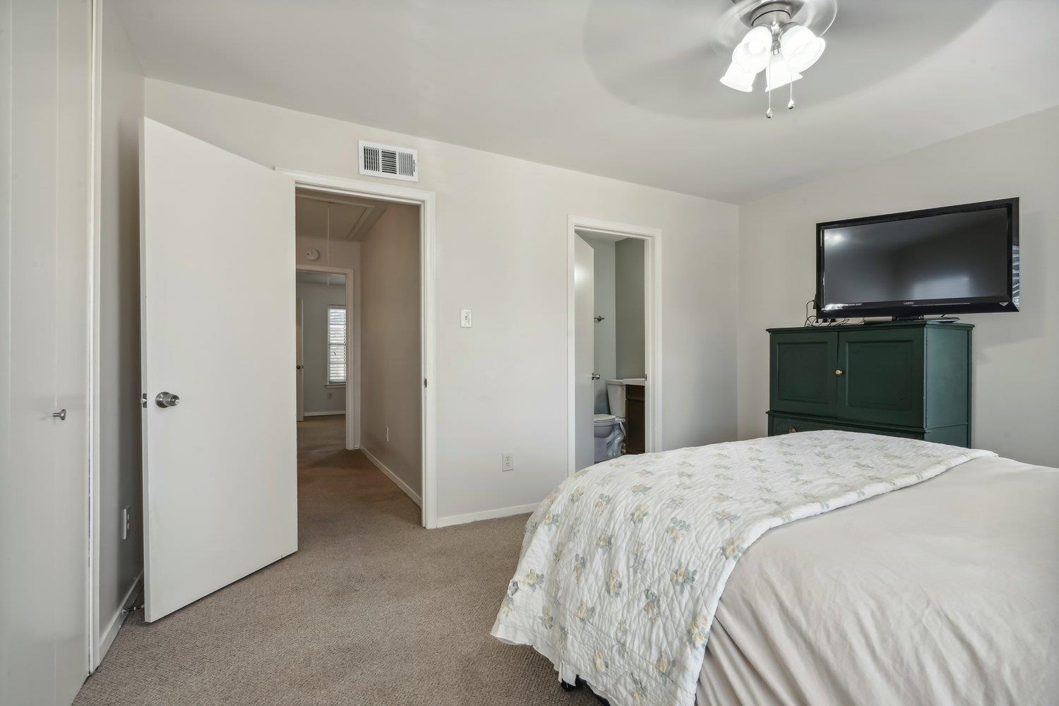 Bedroom with ensuite bath, ceiling fan, and light colored carpet