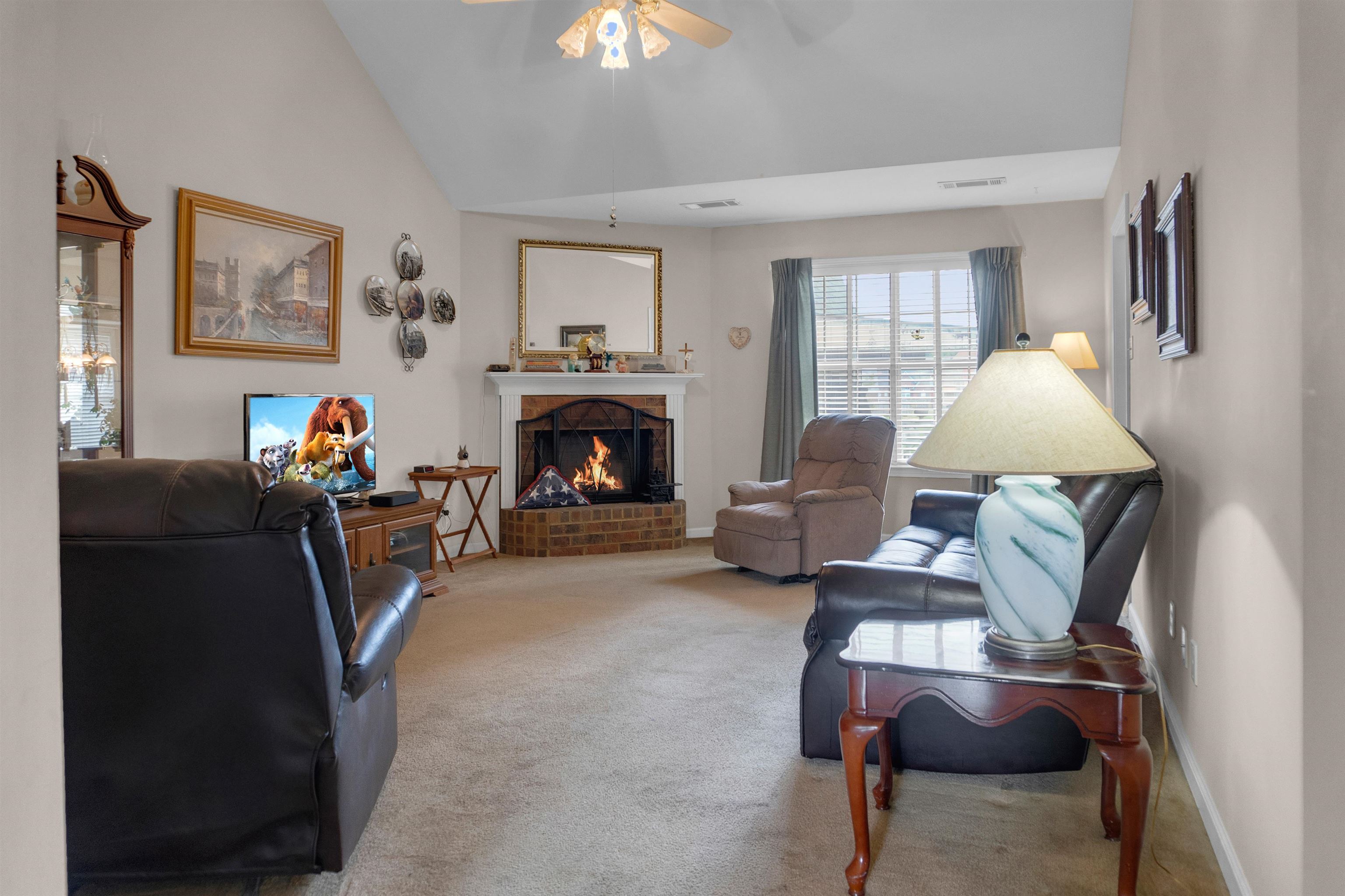 Carpeted living room featuring vaulted ceiling, ceiling fan, and a brick fireplace