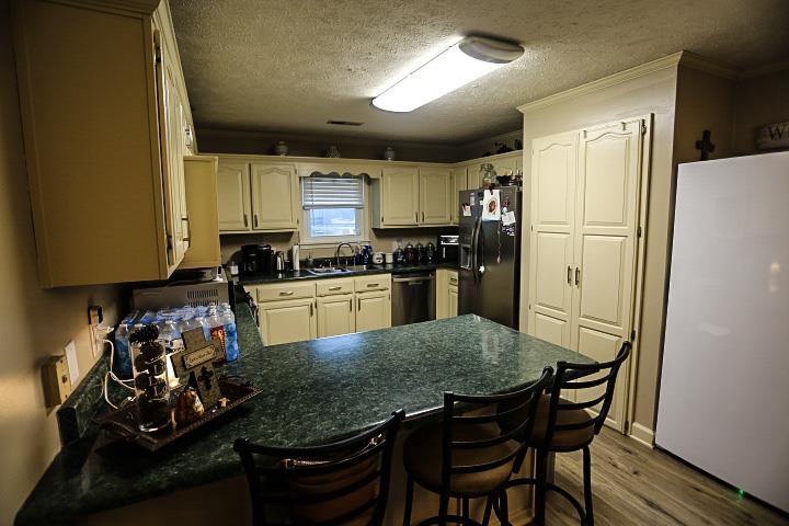 Kitchen featuring kitchen peninsula, wood-type flooring, black refrigerator with ice dispenser, a breakfast bar area, and white fridge