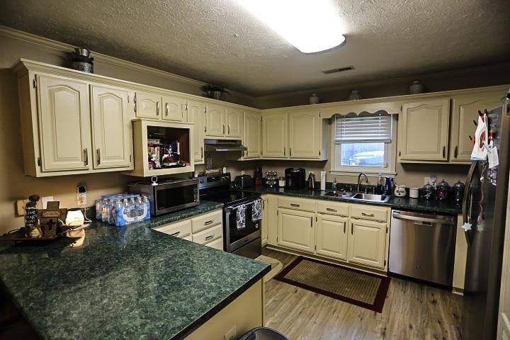 Kitchen featuring appliances with stainless steel finishes, a textured ceiling, light hardwood / wood-style flooring, ornamental molding, and sink