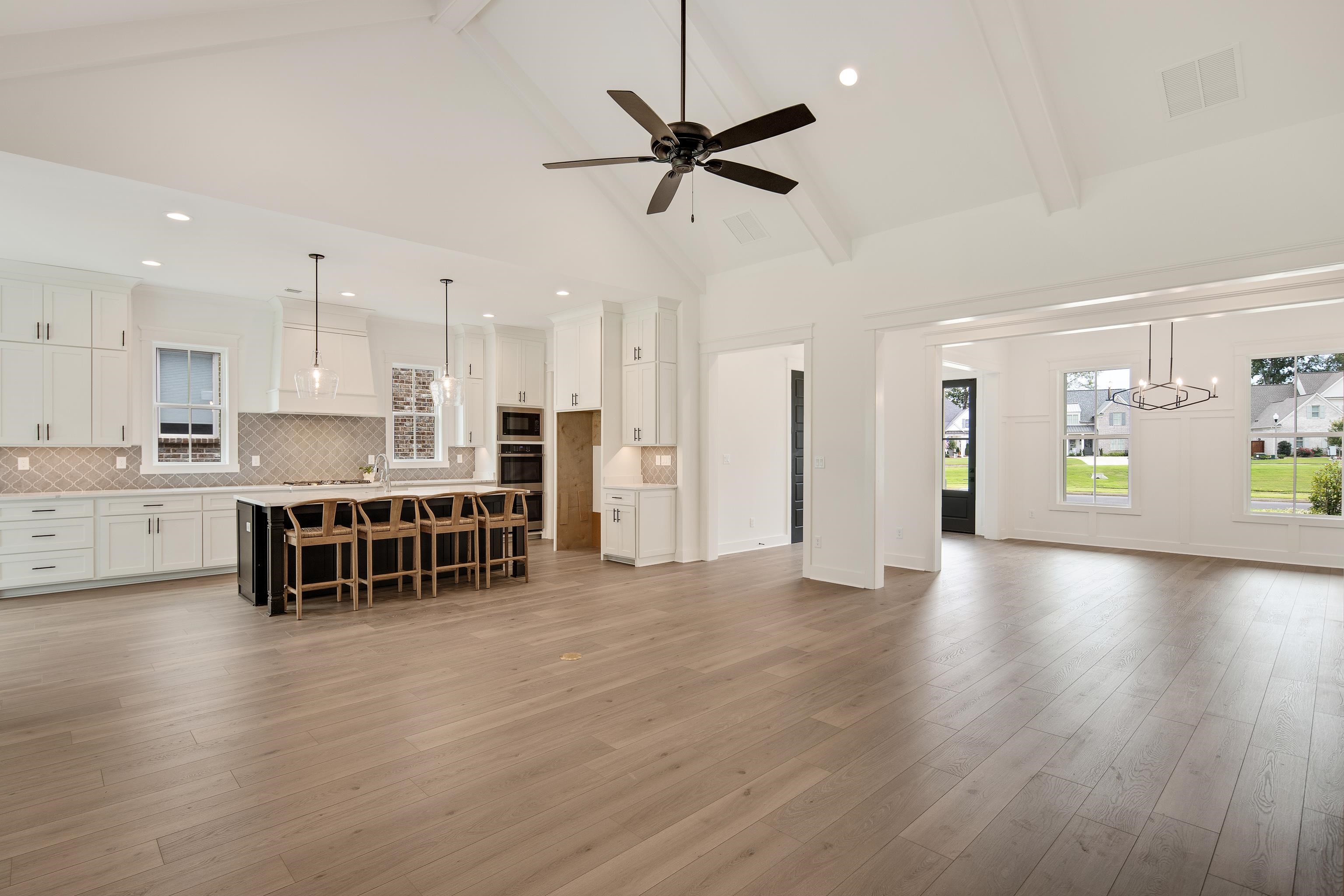 Living room featuring ceiling fan with notable chandelier, light hardwood / wood-style flooring, beamed ceiling, and high vaulted ceiling