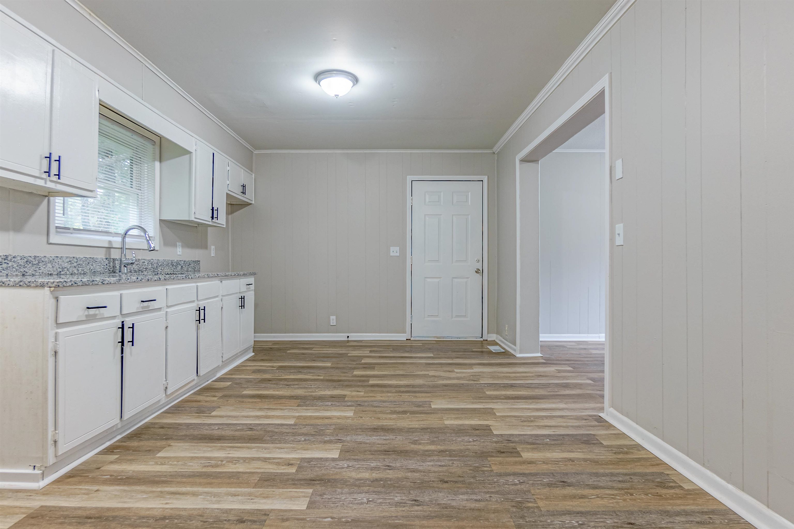 Kitchen with ornamental molding, light hardwood / wood-style floors, white cabinetry, and wood walls