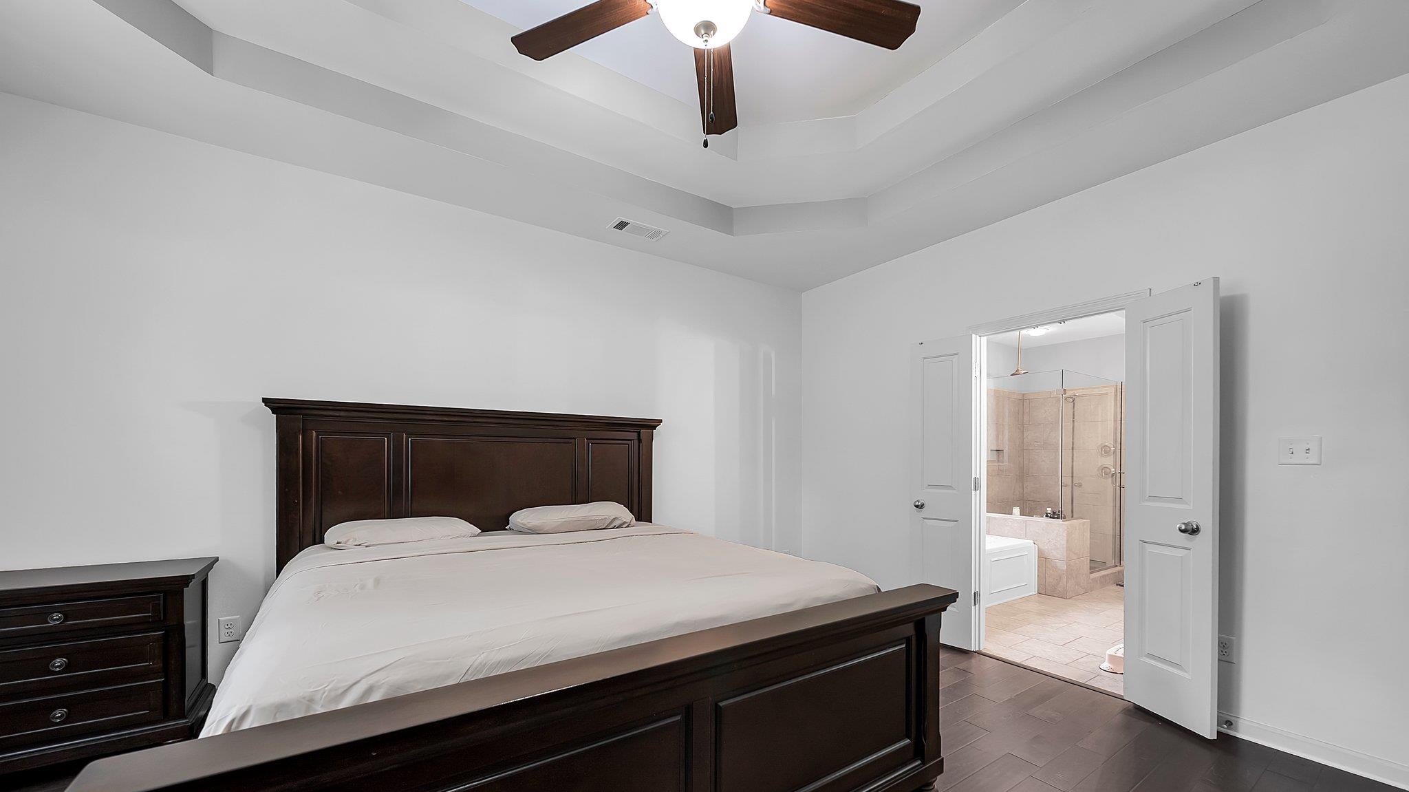 Bedroom featuring ceiling fan, dark wood-type flooring, a raised ceiling, and ensuite bathroom