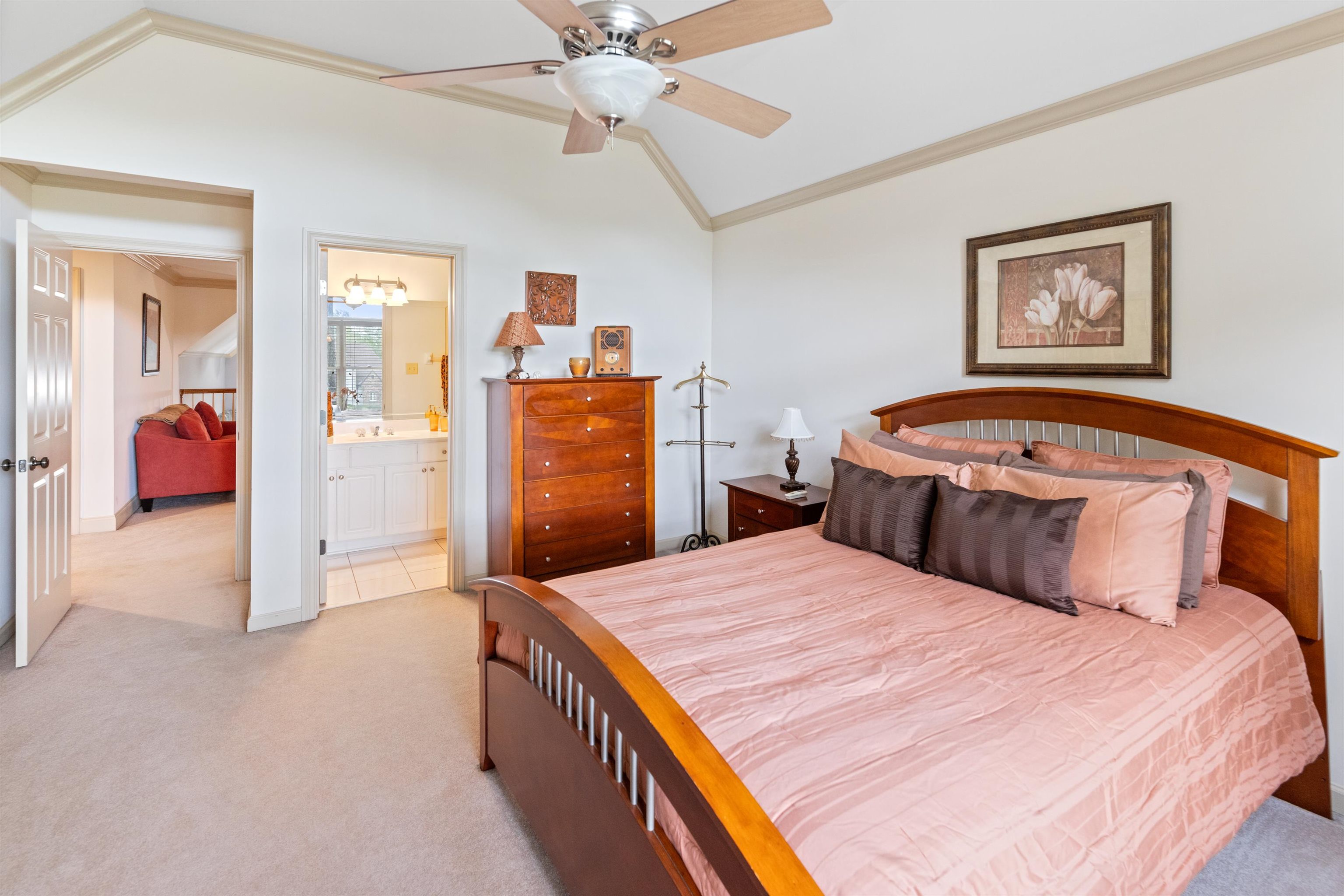 Carpeted bedroom with ceiling fan, lofted ceiling, ensuite bath, and crown molding