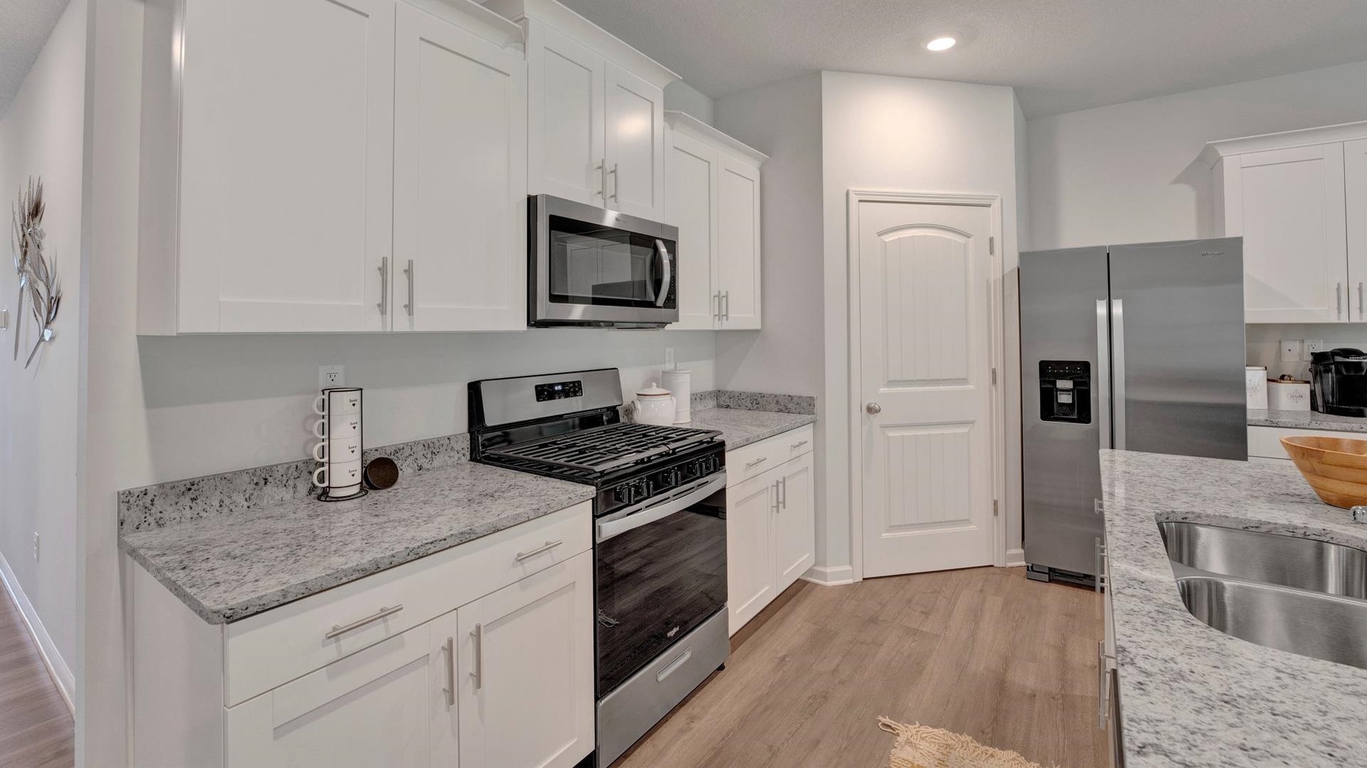 Kitchen with white cabinets, light wood-type flooring, light stone counters, and stainless steel appliances