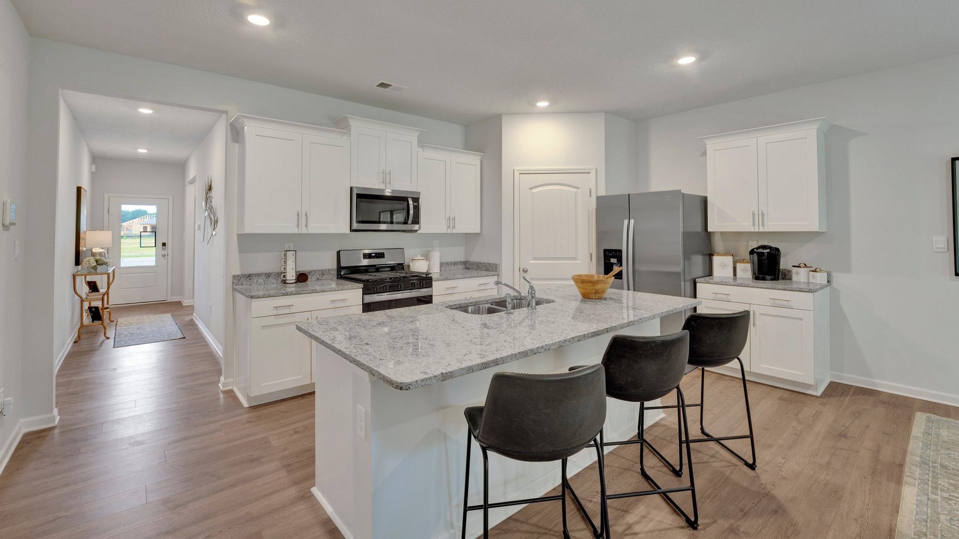 Kitchen with white cabinets, light hardwood / wood-style flooring, a center island with sink, and stainless steel appliances