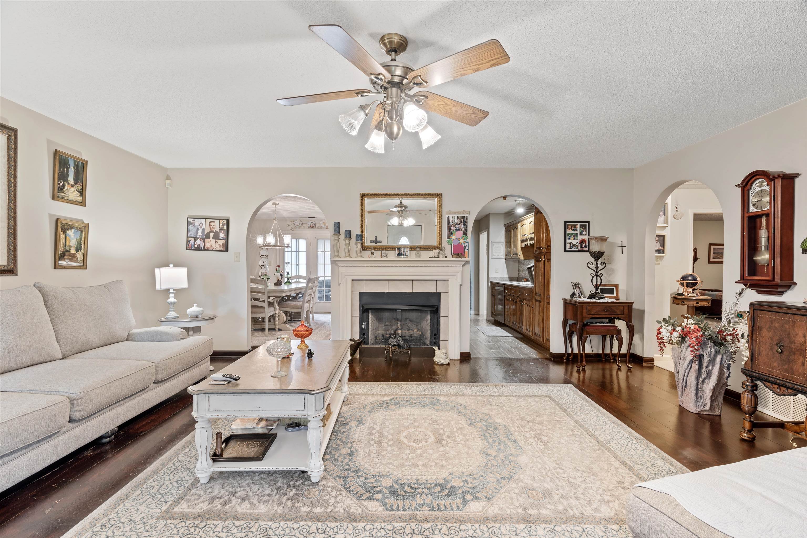 Living room with a fireplace, dark wood-type flooring, and ceiling fan