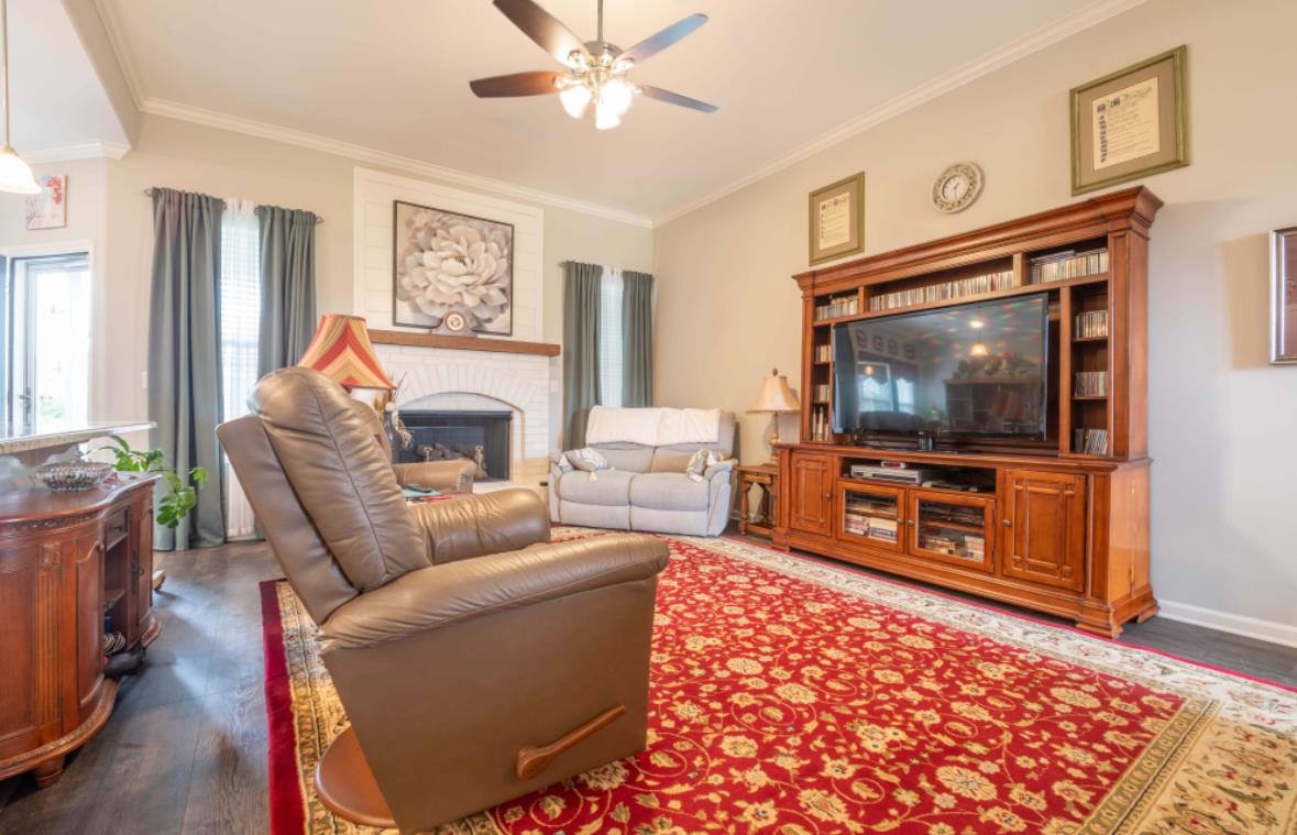 Living room with ceiling fan, a fireplace, dark wood-type flooring, and crown molding