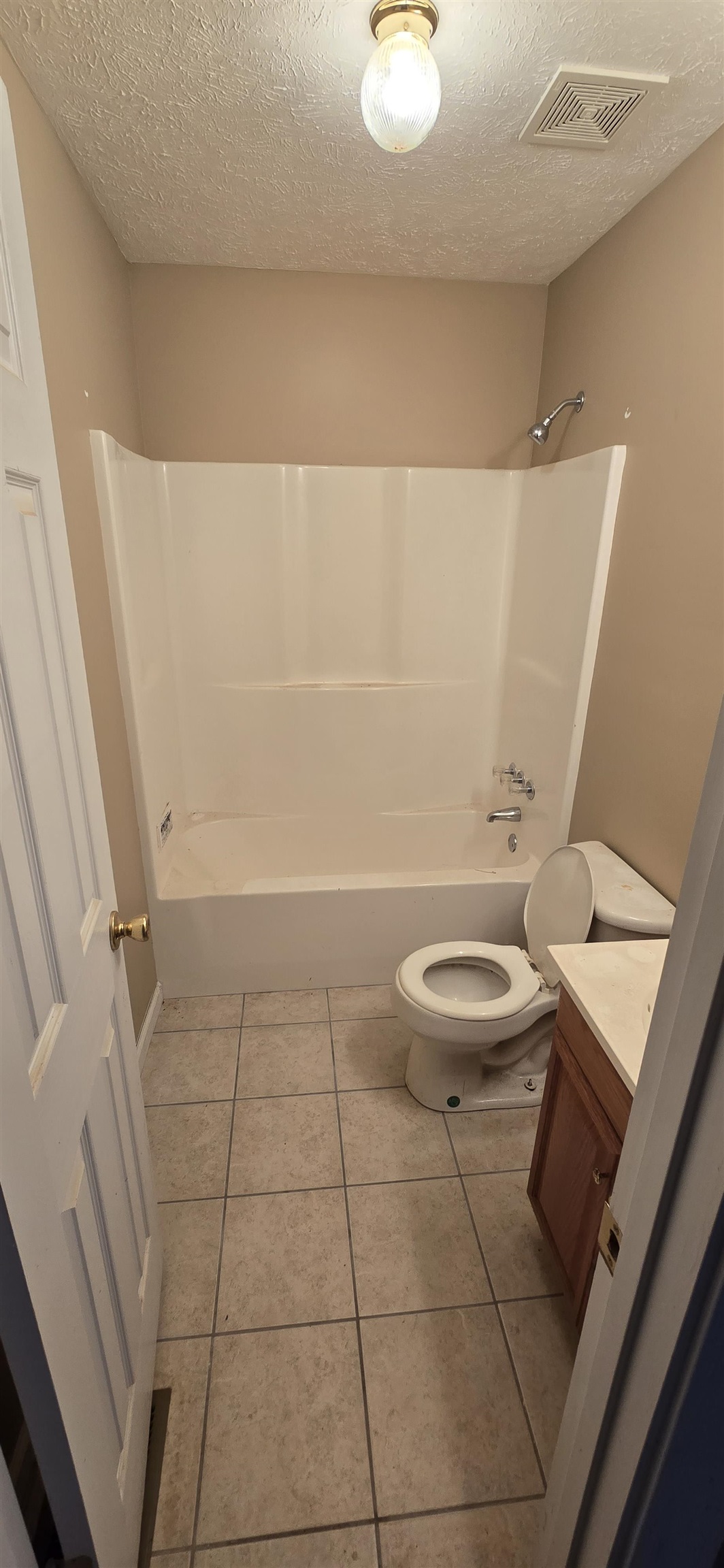 Full bathroom featuring a textured ceiling, vanity, toilet, and  shower combination