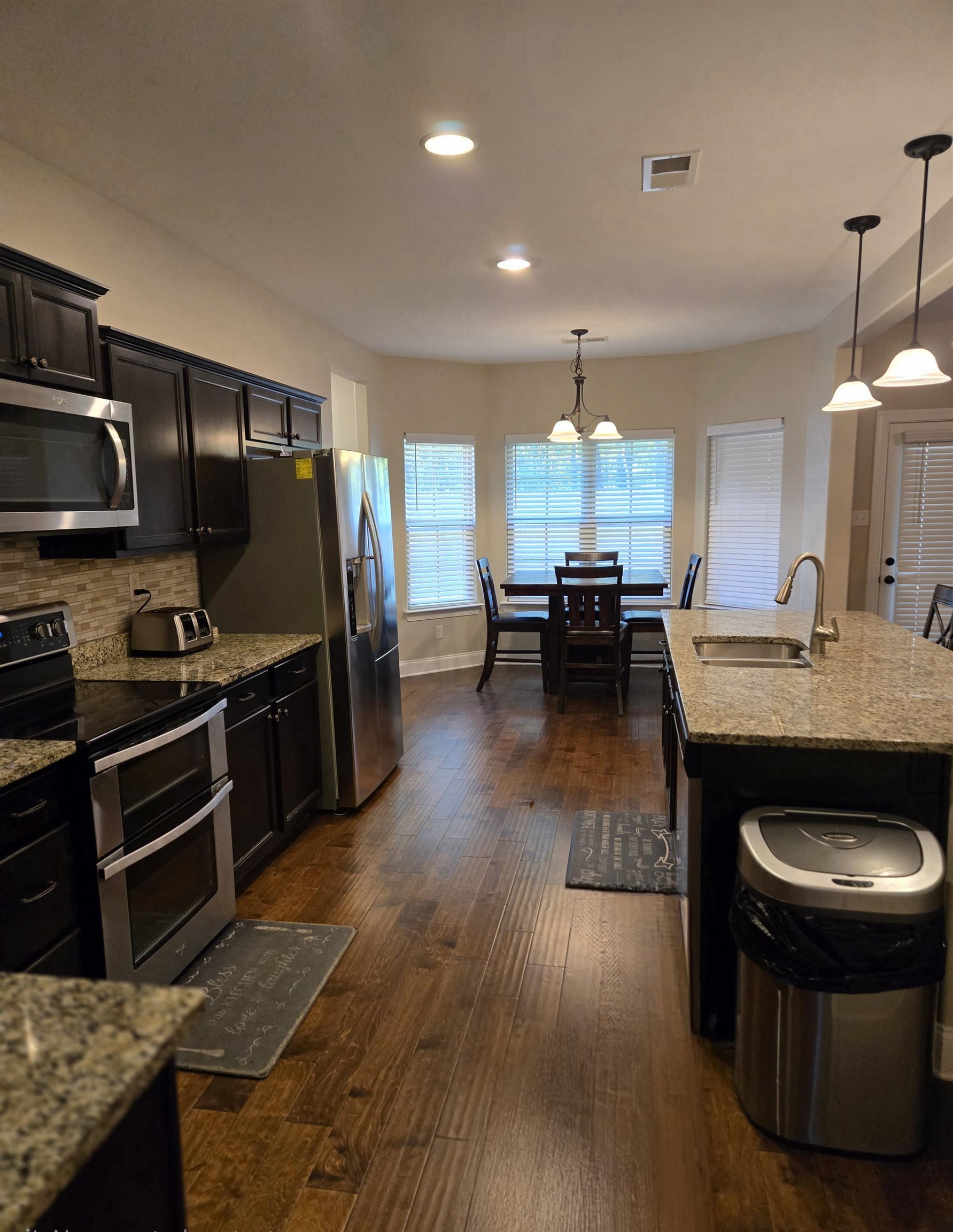 Kitchen with appliances with stainless steel finishes, sink, pendant lighting, and light stone counters