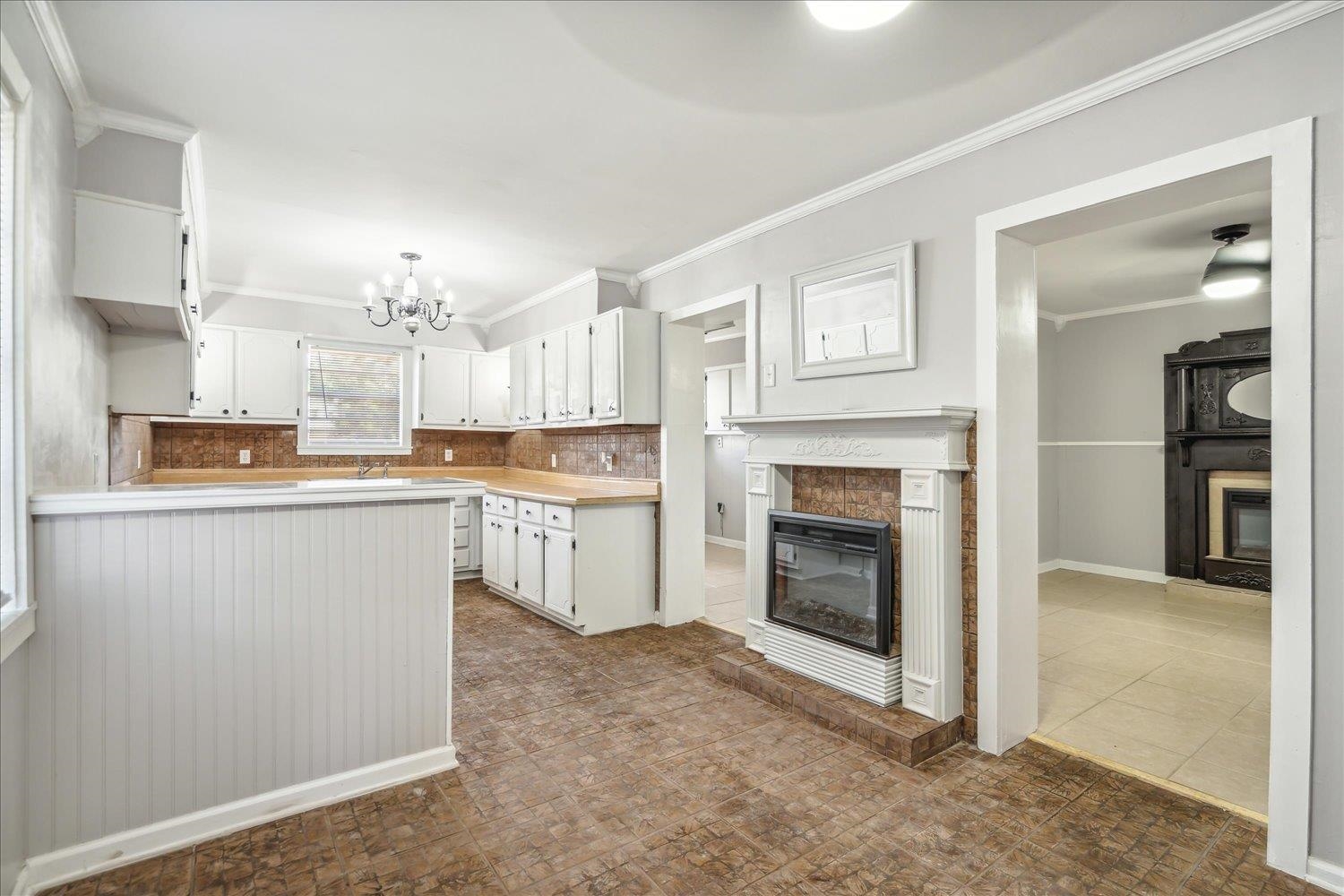 Kitchen featuring a notable chandelier, white cabinetry, a tile fireplace, and tasteful backsplash