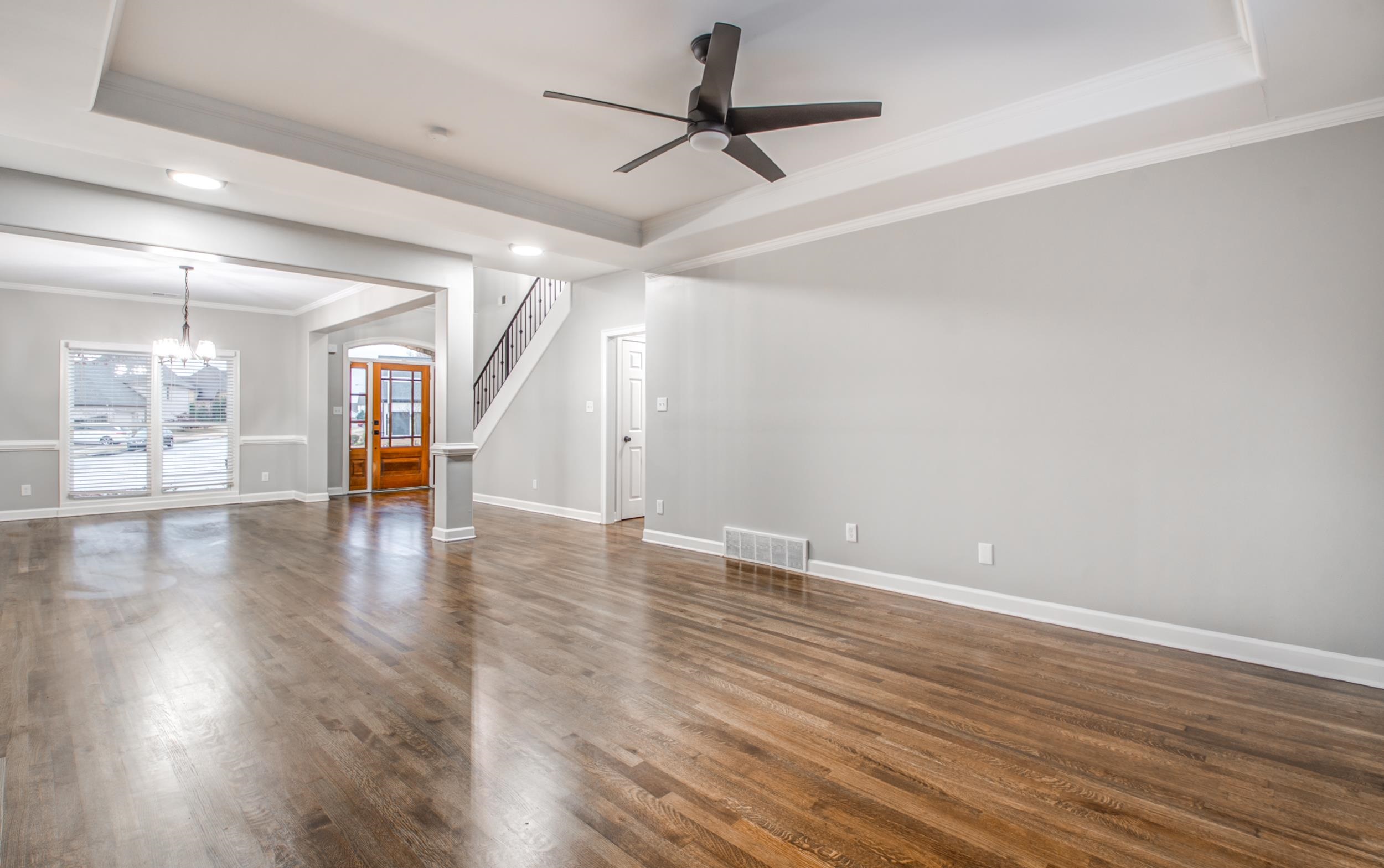 Unfurnished living room featuring ceiling fan with notable chandelier, a tray ceiling, crown molding, and dark hardwood / wood-style flooring