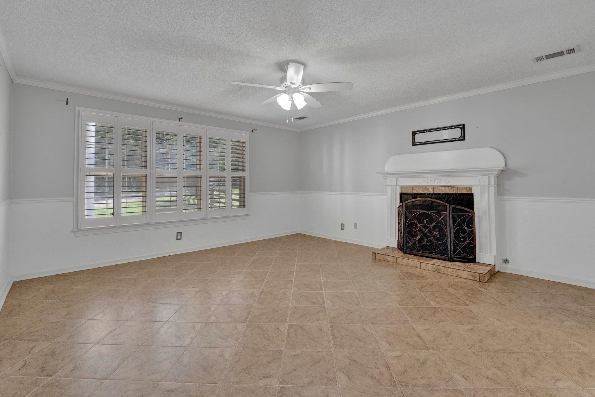 Unfurnished living room with ornamental molding, a textured ceiling, a tile fireplace, and ceiling fan