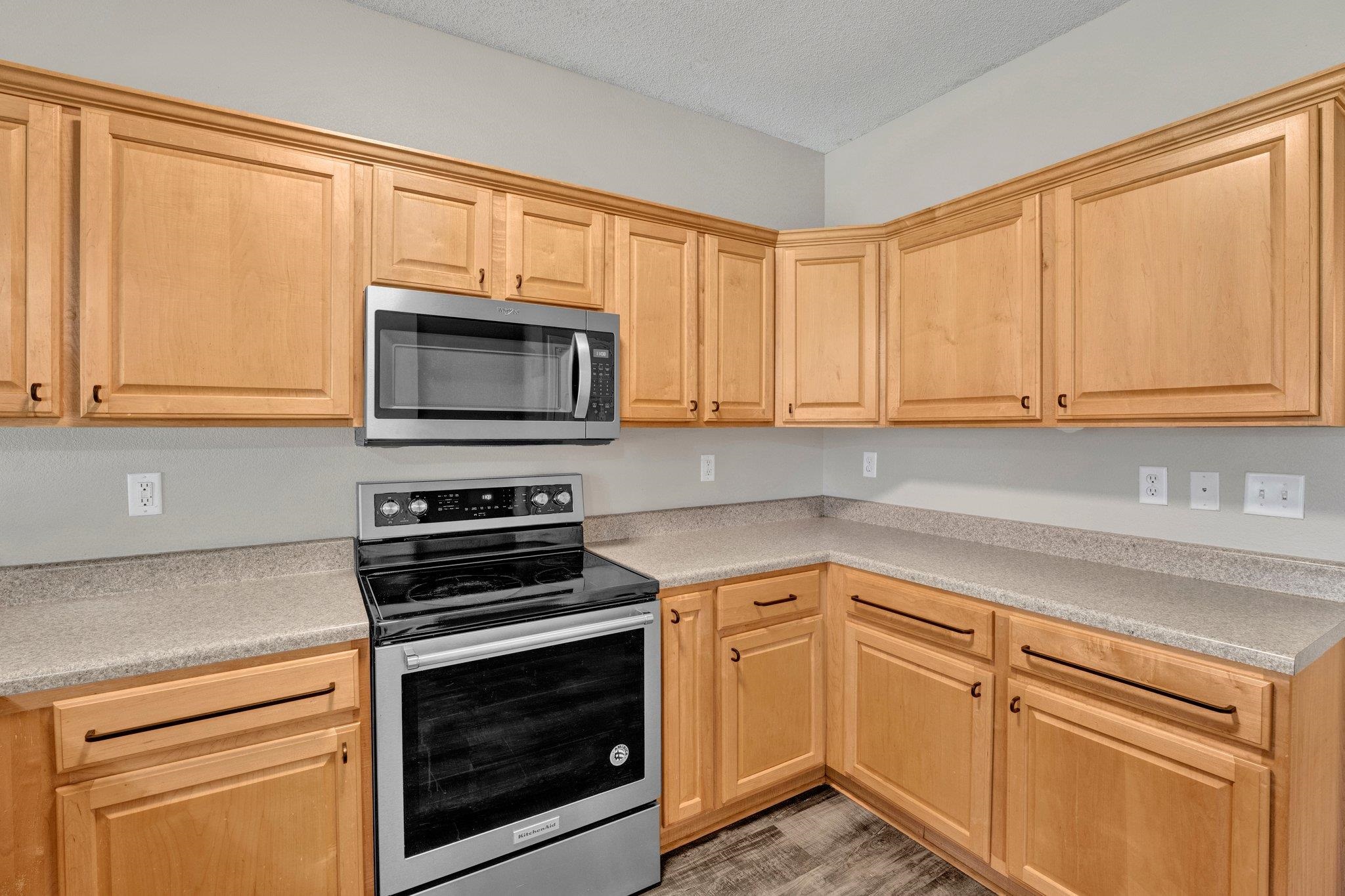 Kitchen featuring light brown cabinetry, a textured ceiling, appliances with stainless steel finishes, and hardwood / wood-style flooring