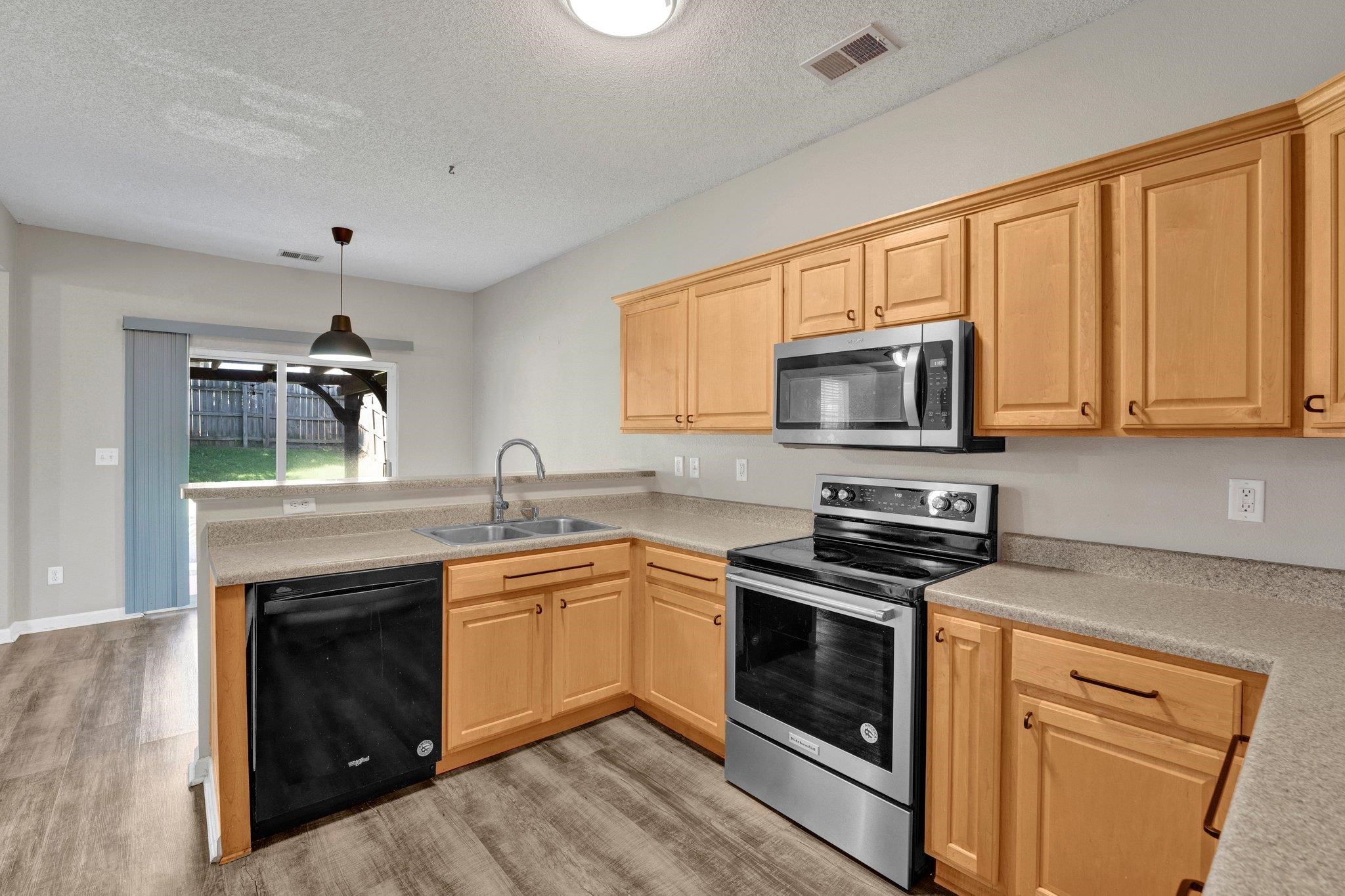 Kitchen with pendant lighting, light wood-type flooring, sink, appliances with stainless steel finishes, and light brown cabinetry