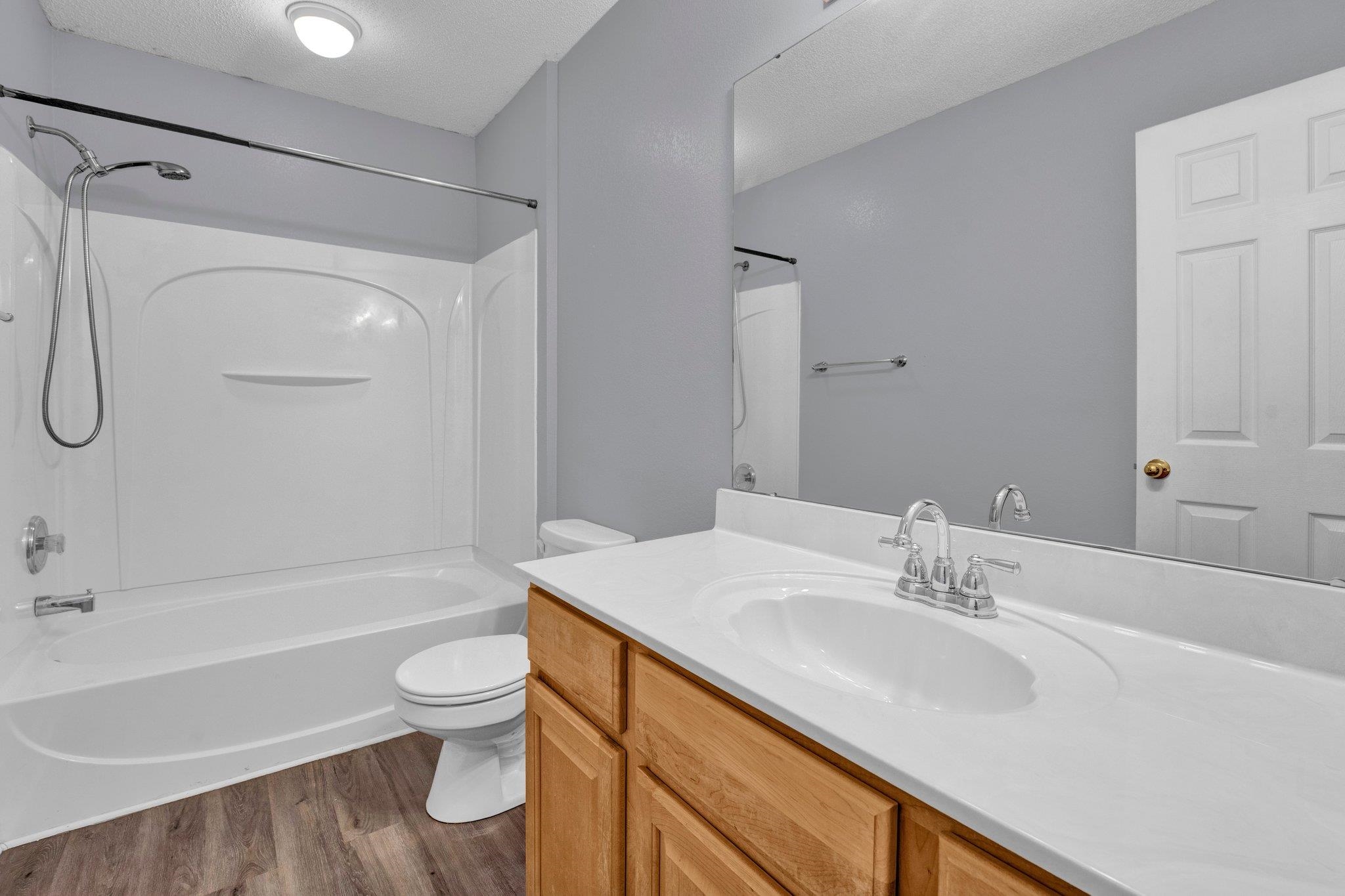 Full bathroom with a textured ceiling, hardwood / wood-style flooring, washtub / shower combination, vanity, and toilet