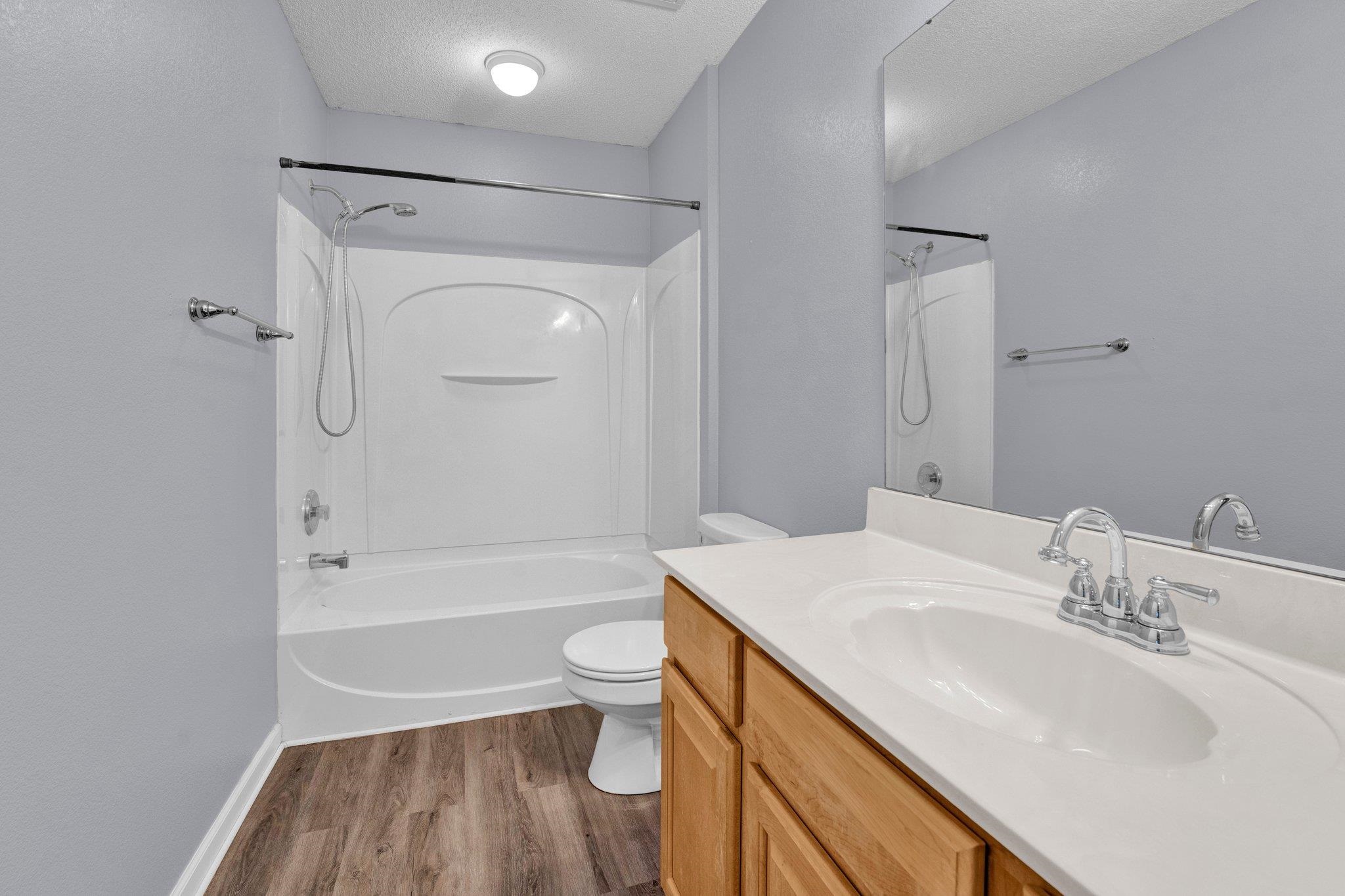 Full bathroom with vanity, a textured ceiling, hardwood / wood-style flooring, shower / tub combination, and toilet