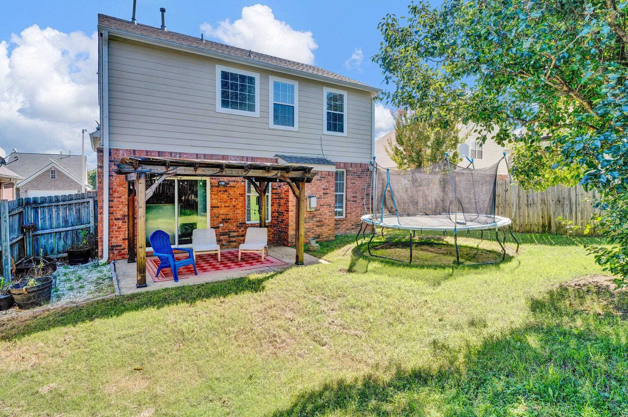 Rear view of house featuring a pergola, a trampoline, a lawn, and a patio