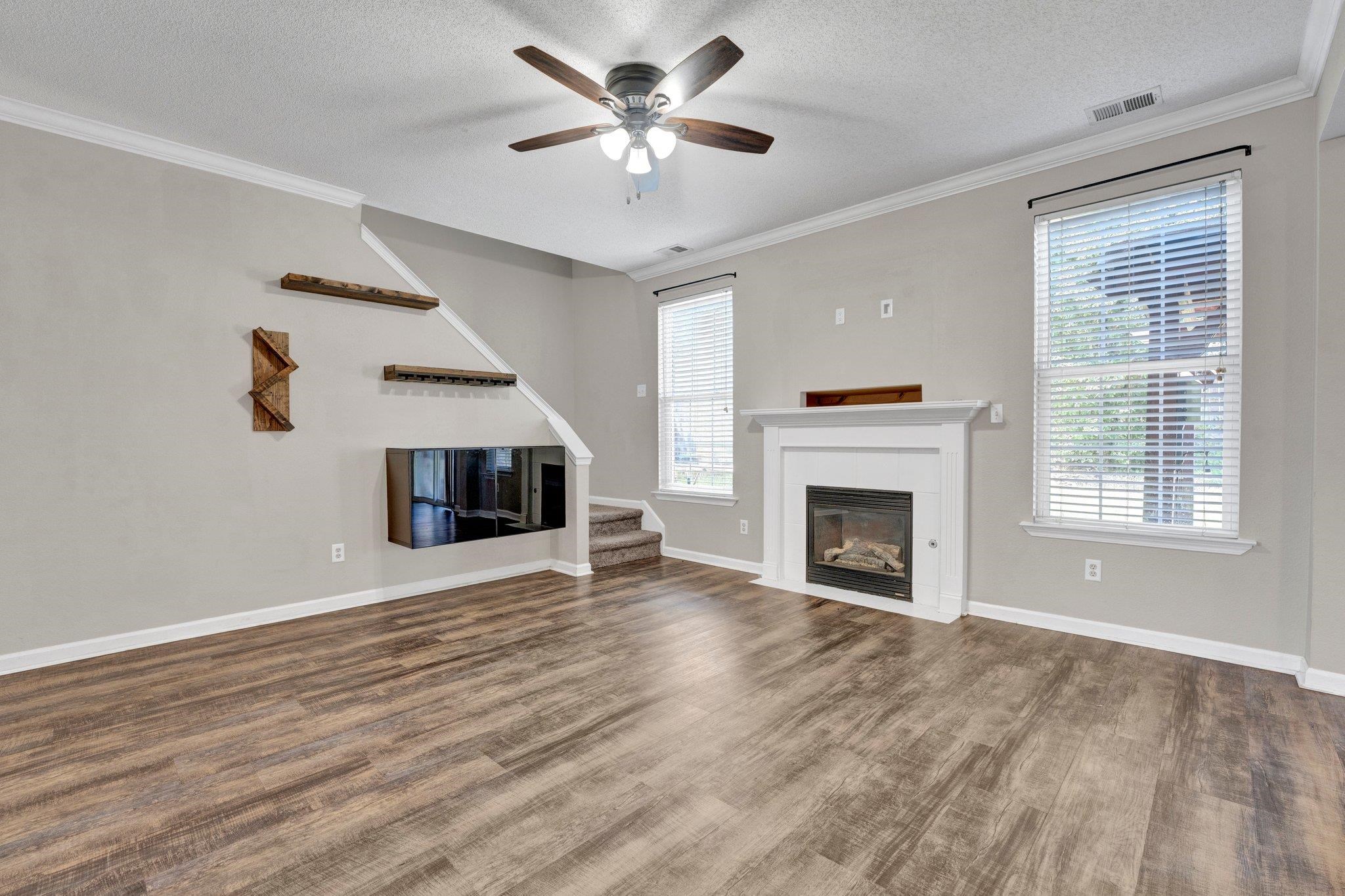 Unfurnished living room featuring ceiling fan, ornamental molding, a textured ceiling, and hardwood / wood-style floors