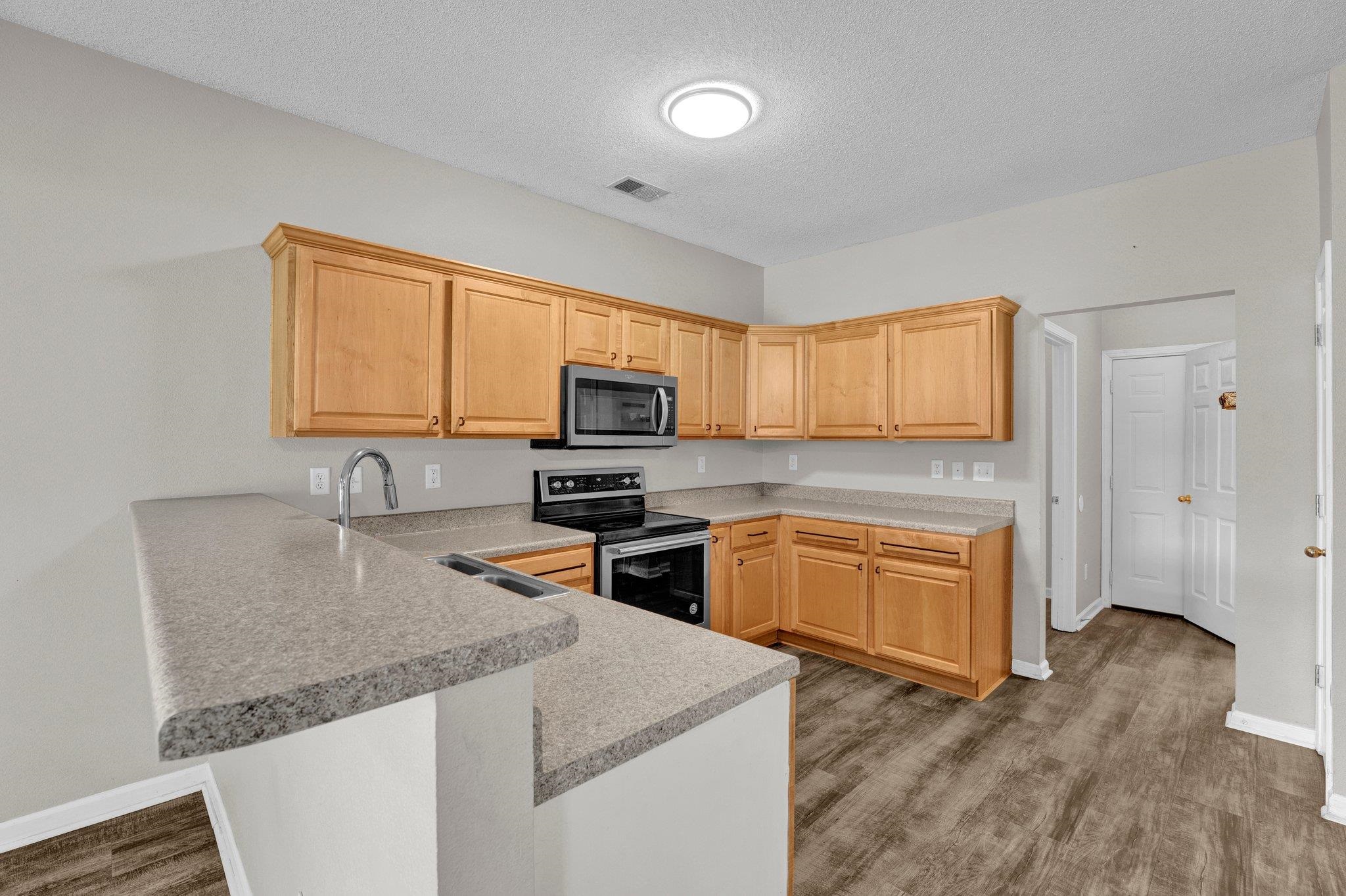 Kitchen featuring light hardwood / wood-style floors, a textured ceiling, stainless steel appliances, and kitchen peninsula
