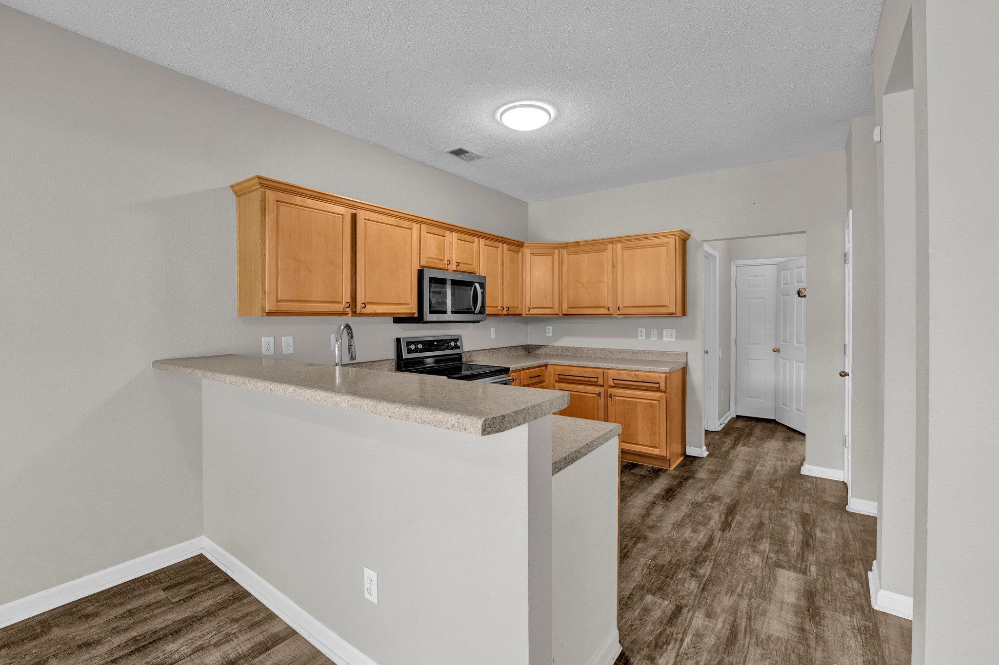 Kitchen featuring sink, kitchen peninsula, a textured ceiling, dark wood-type flooring, and stainless steel appliances