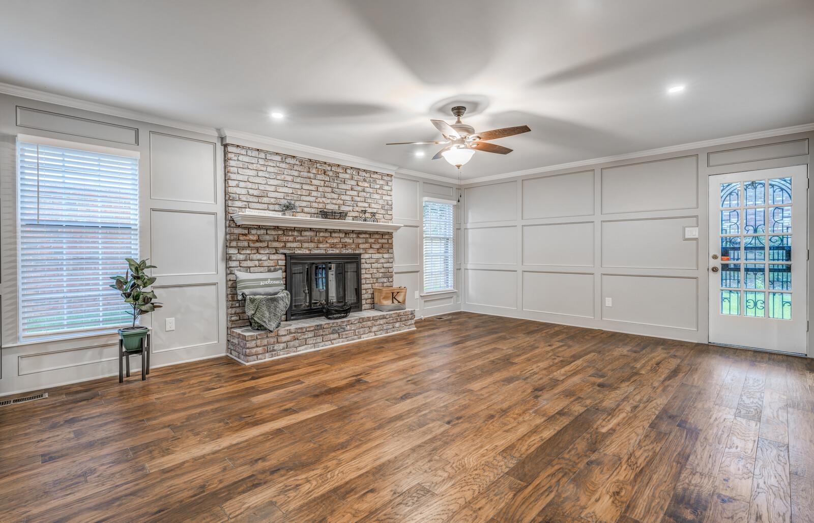 Unfurnished living room featuring ceiling fan, a brick fireplace, crown molding, and dark wood-type flooring