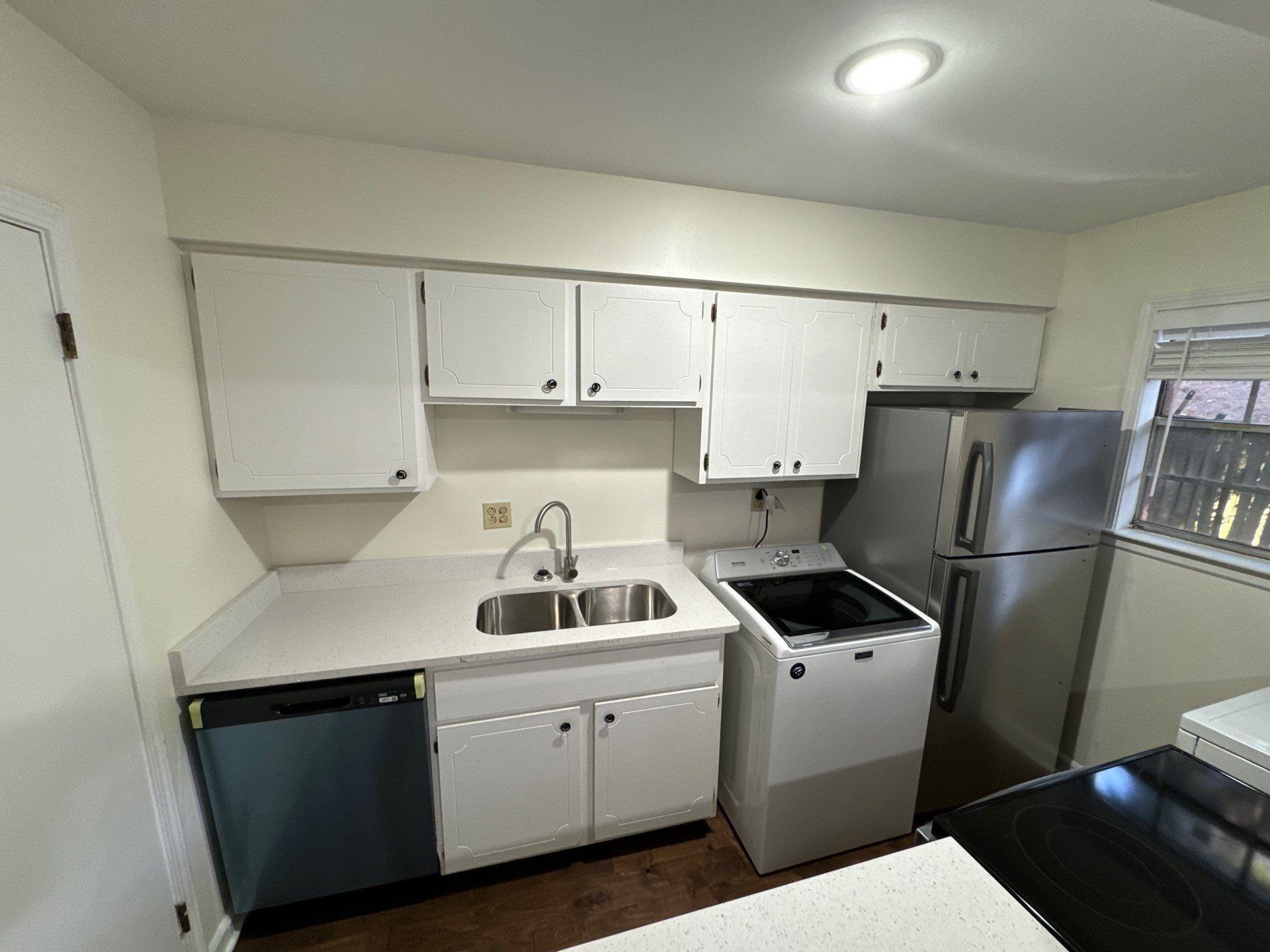 Kitchen featuring appliances with stainless steel finishes, washer / clothes dryer, white cabinetry, dark wood-type flooring, and sink