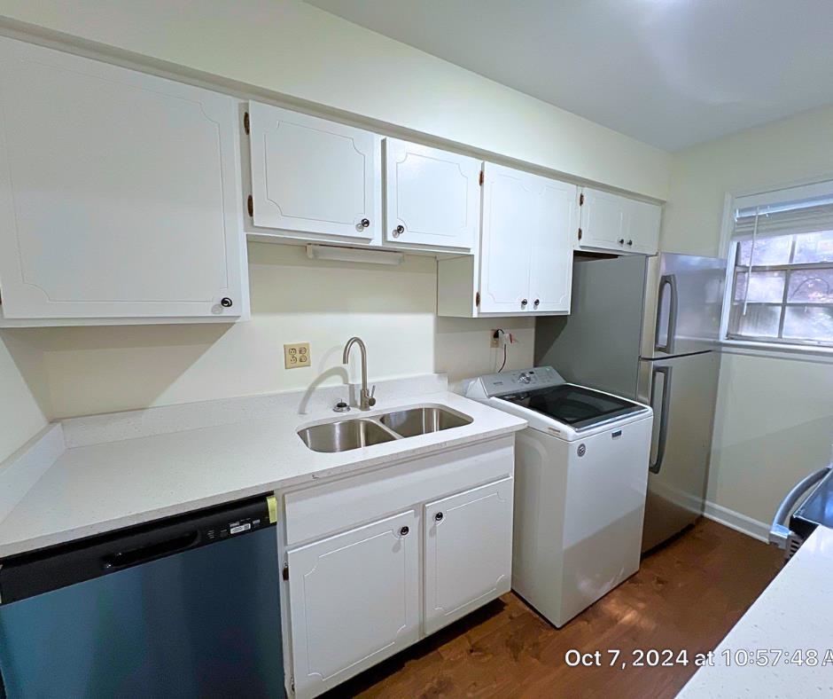 Kitchen with white cabinets, sink, stainless steel dishwasher, dark hardwood / wood-style floors, and washer / dryer