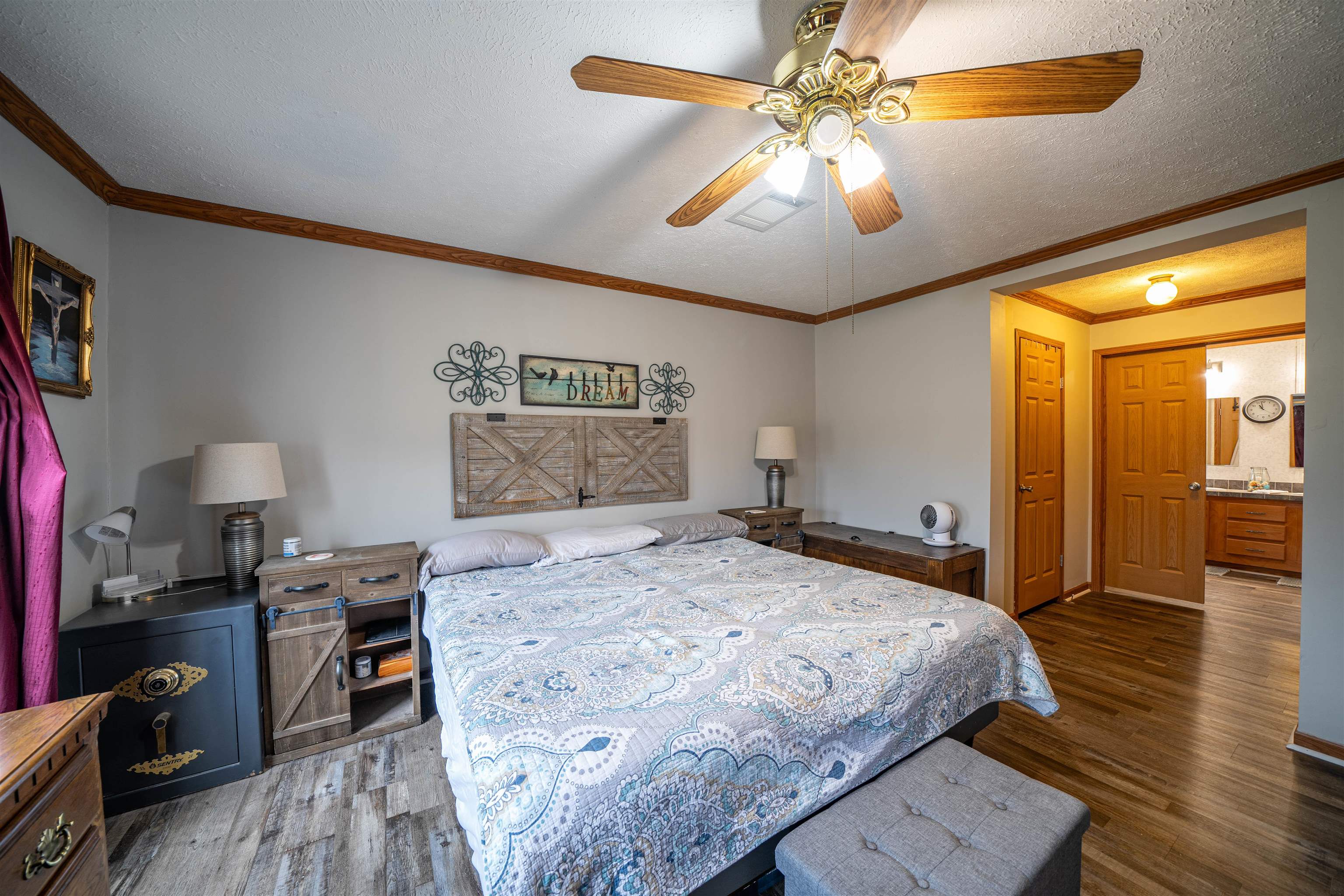 Bedroom with ceiling fan, ornamental molding, a textured ceiling, dark wood-type flooring, and ensuite bath