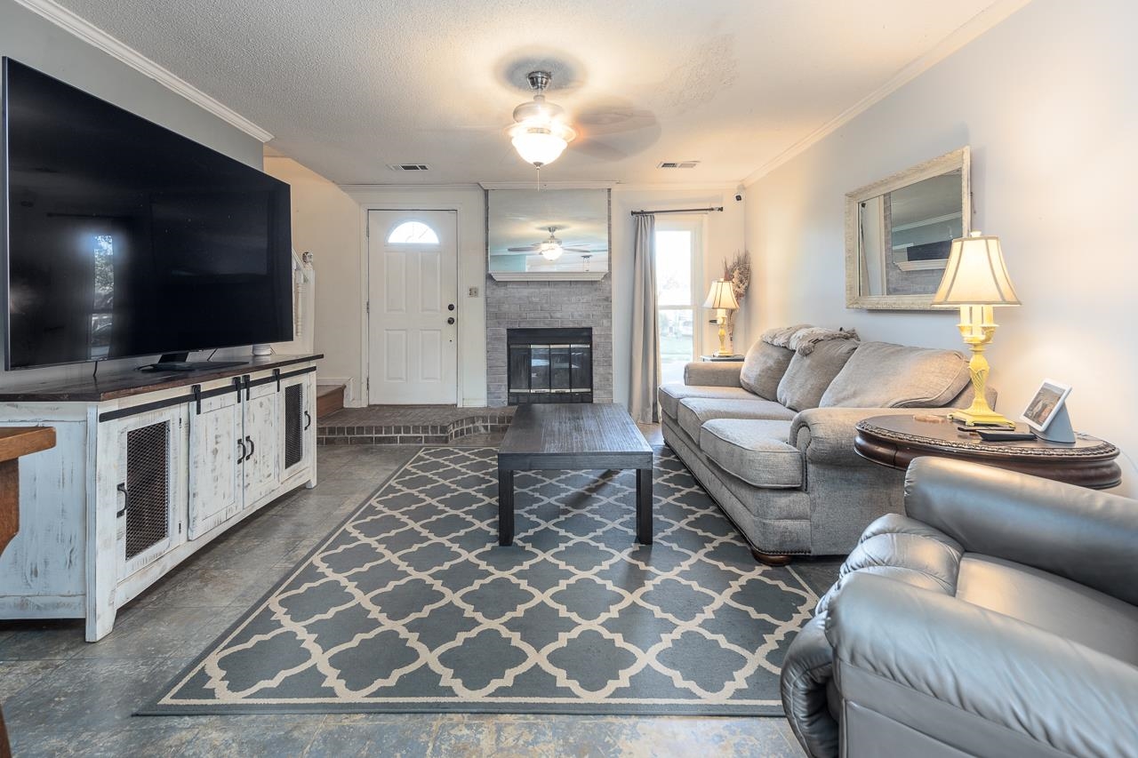 Living room with a textured ceiling, a fireplace, ornamental molding, and ceiling fan