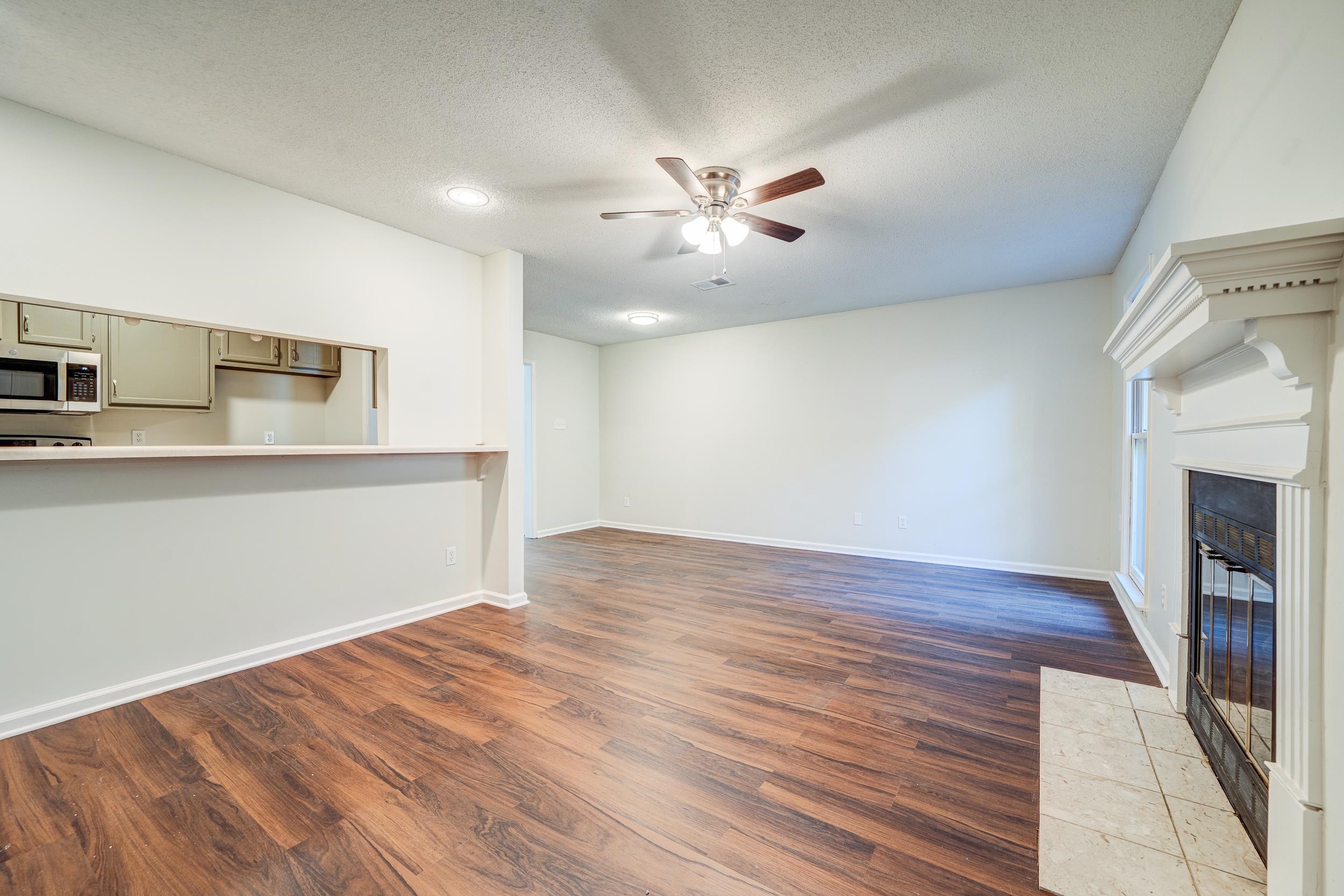 Unfurnished living room featuring ceiling fan, a textured ceiling, a tiled fireplace, and dark hardwood / wood-style flooring