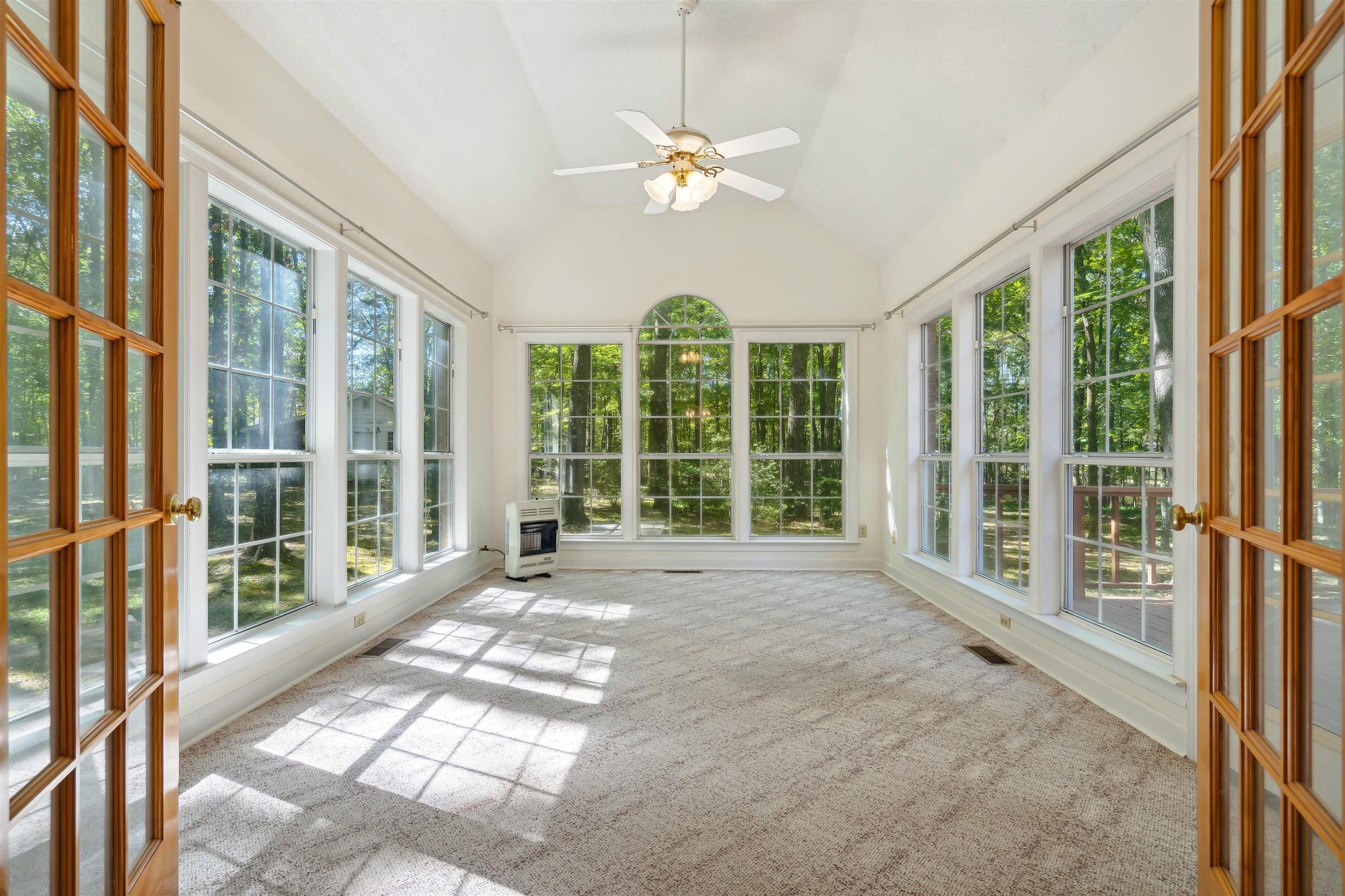 Unfurnished sunroom with heating unit, vaulted ceiling, ceiling fan, and a wood stove