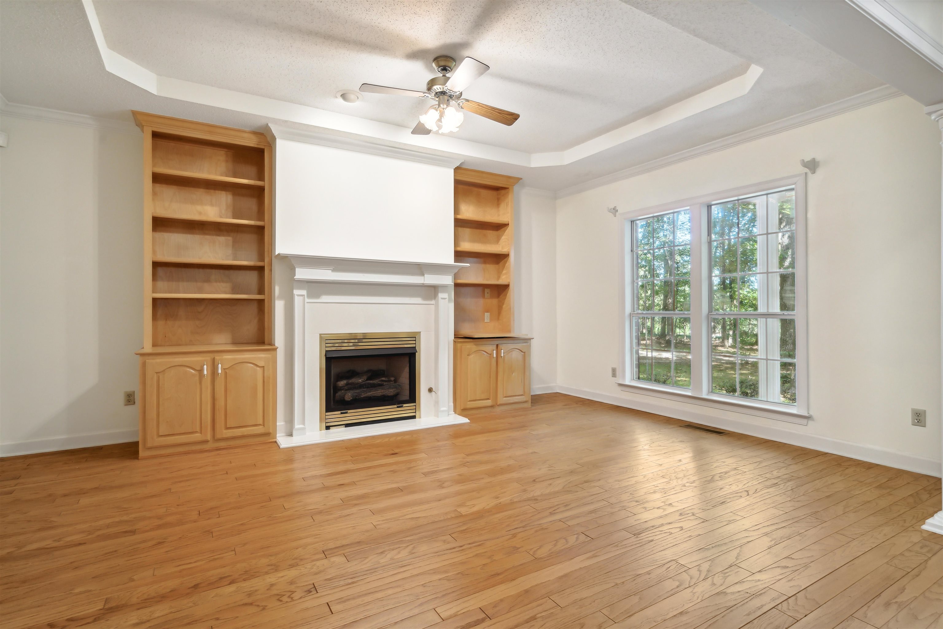 Unfurnished living room featuring ceiling fan, light wood-type flooring, crown molding, and a raised ceiling