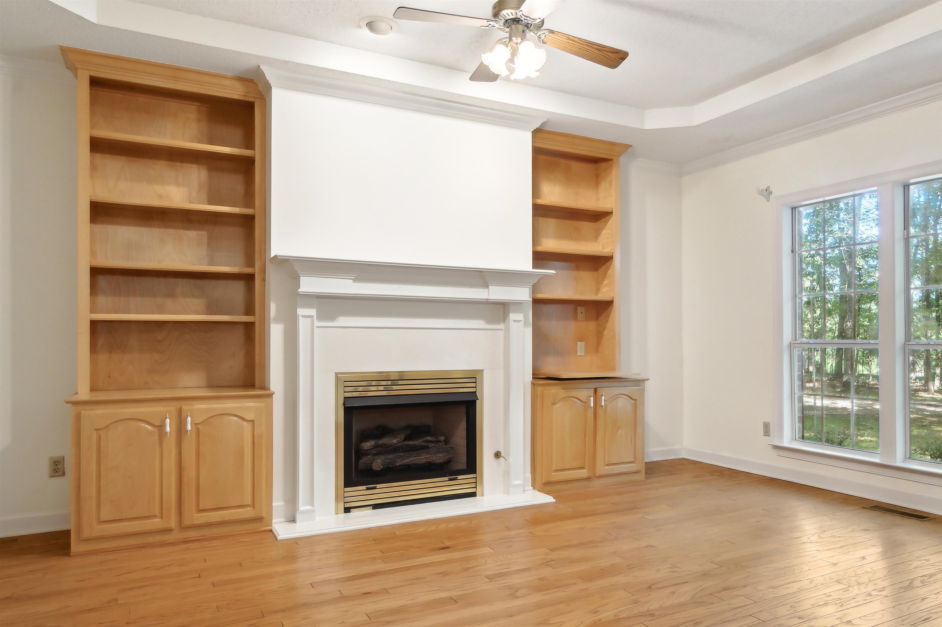 Unfurnished living room with a raised ceiling, ornamental molding, ceiling fan, and light hardwood / wood-style flooring
