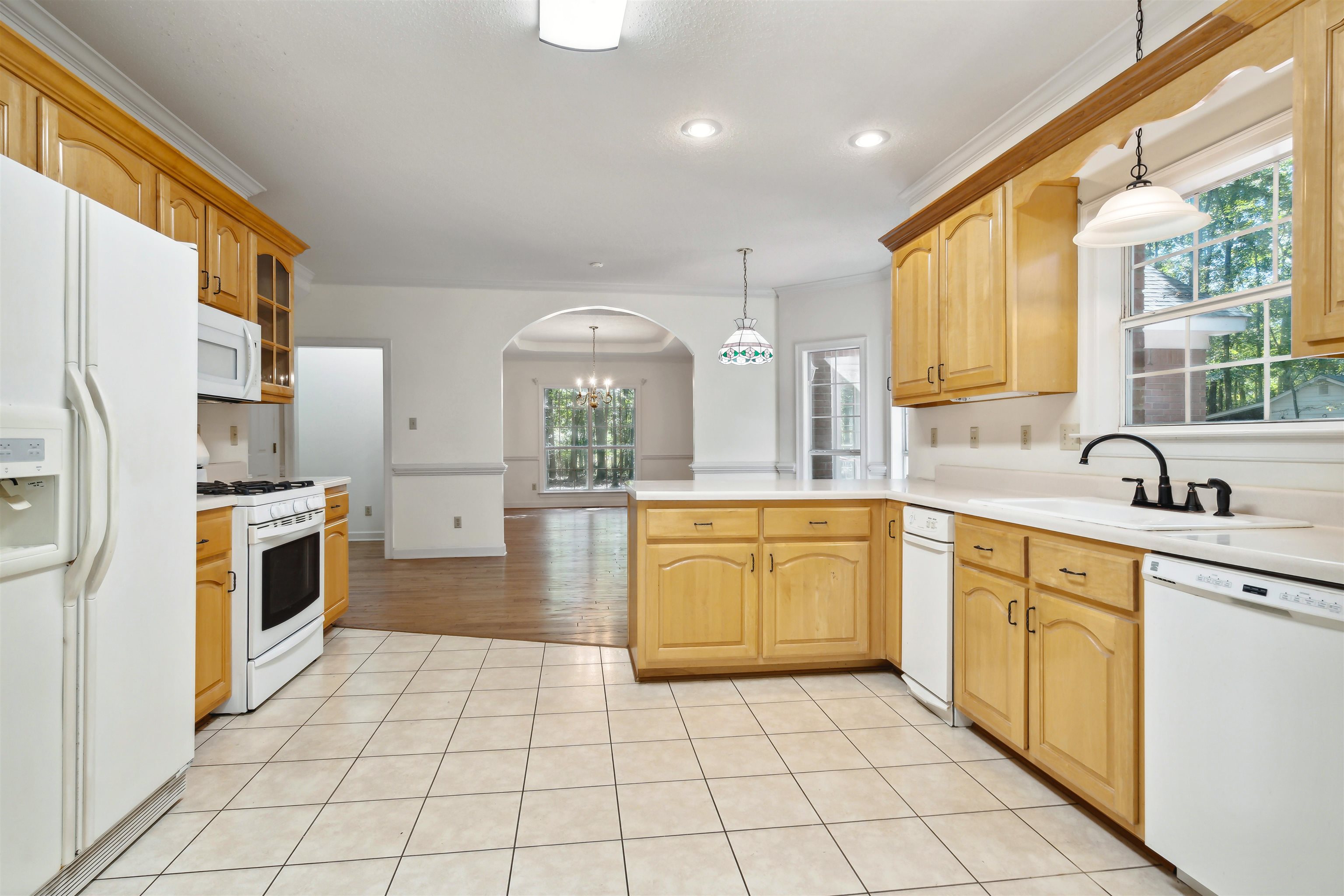 Kitchen with a wealth of natural light, white appliances, and hanging light fixtures