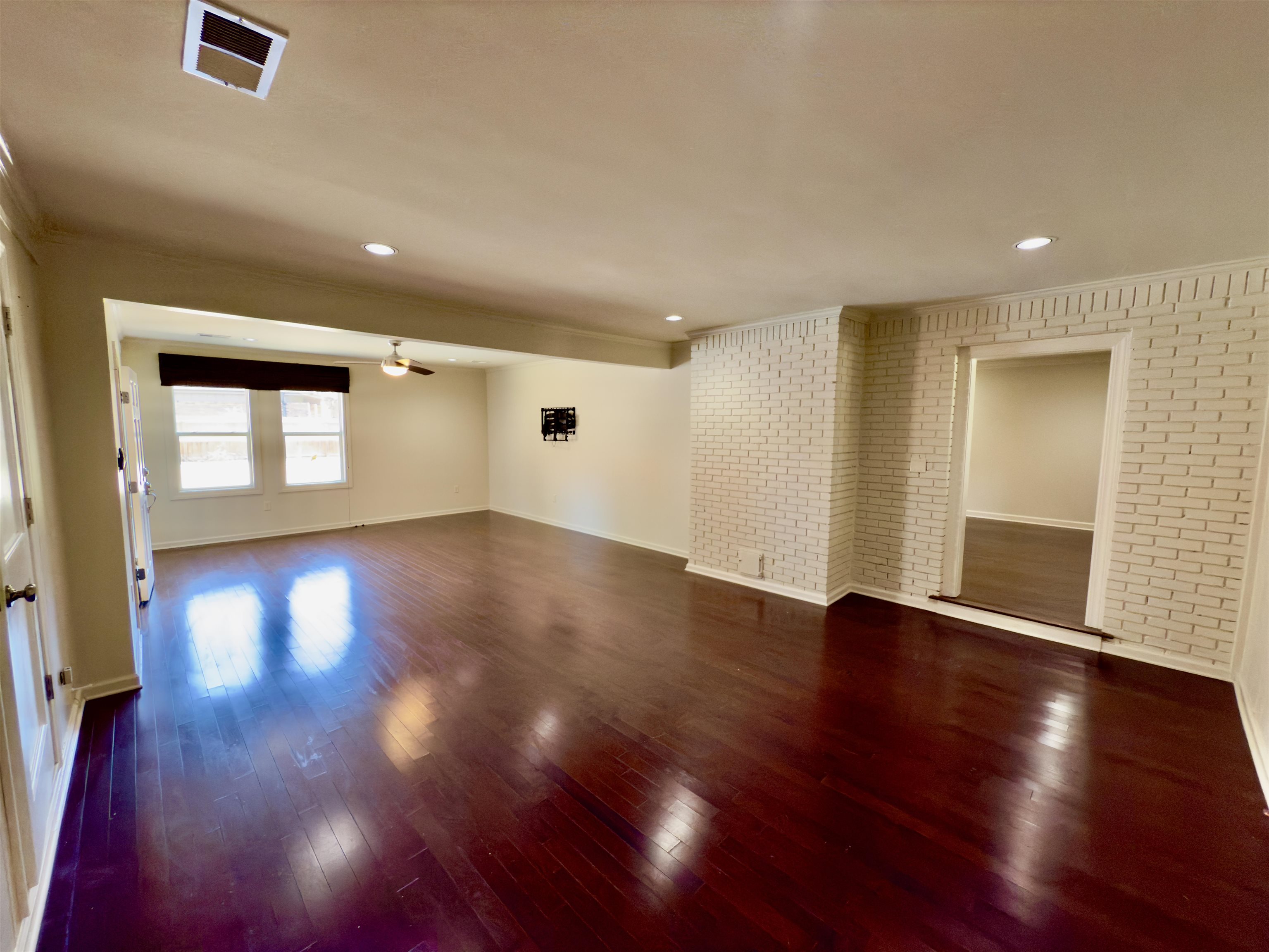 Unfurnished living room featuring brick wall, dark hardwood / wood-style flooring, and ceiling fan