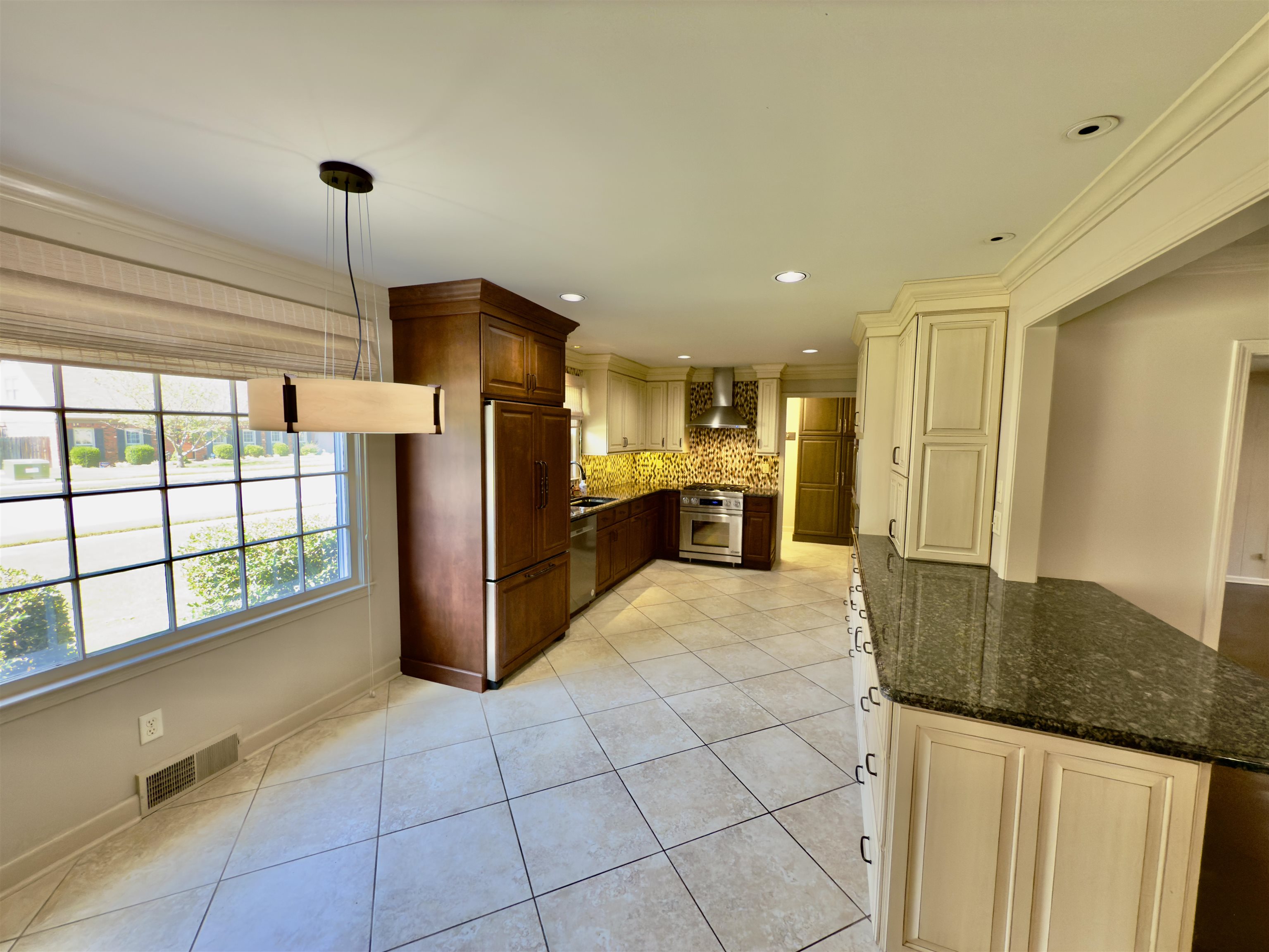 Kitchen featuring wall chimney exhaust hood, premium appliances, tasteful backsplash, dark stone counters, and sink. Updated 2014