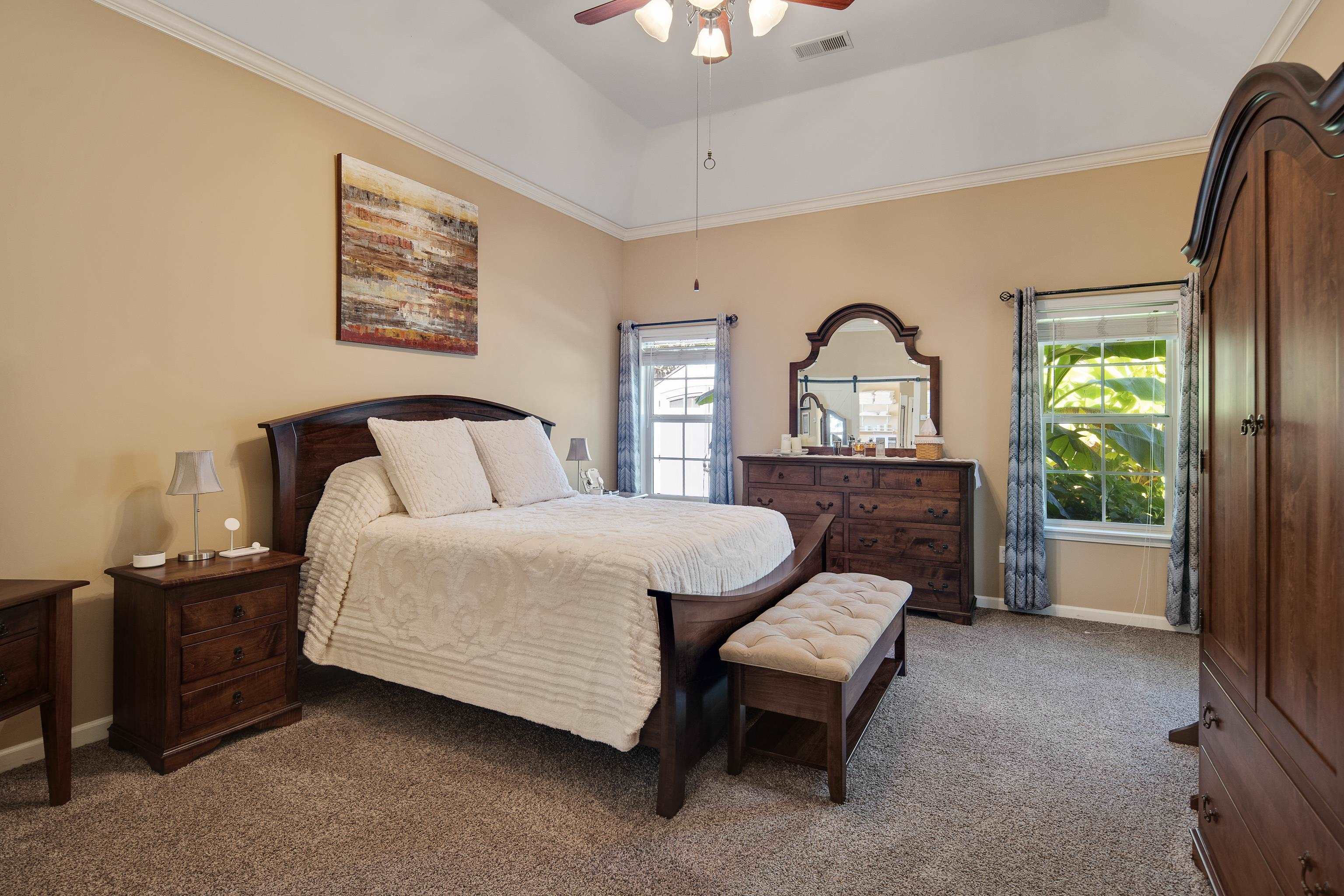 Carpeted bedroom featuring ornamental molding, multiple windows, ceiling fan, and a tray ceiling