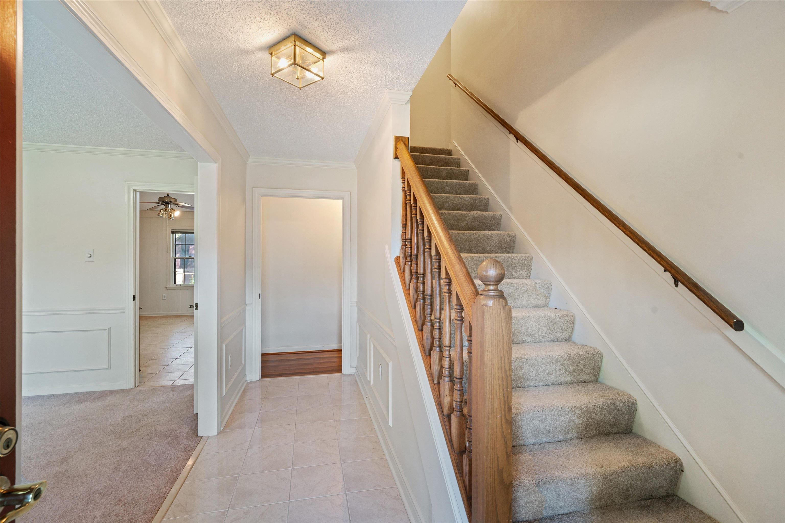 Stairway with a textured ceiling, ceiling fan, ornamental molding, and carpet flooring