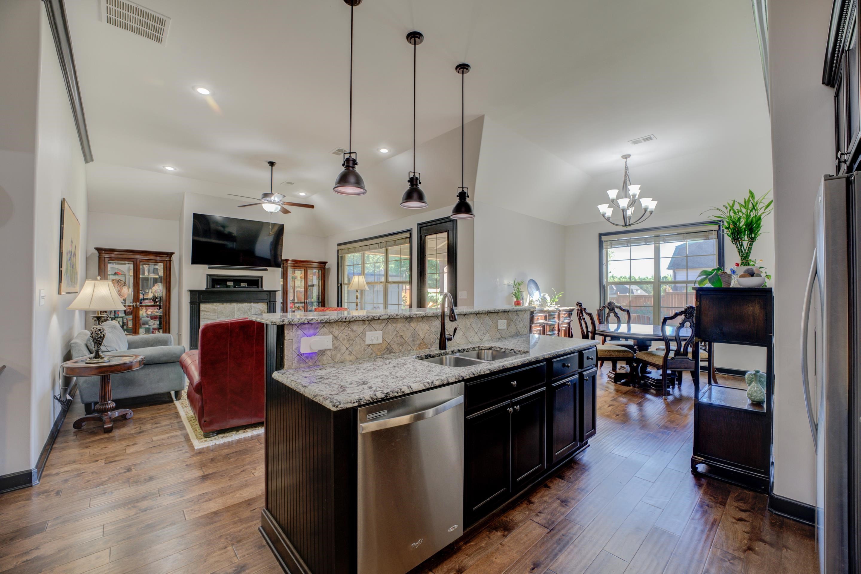 Kitchen with dark wood-type flooring, decorative light fixtures, sink, stainless steel appliances, and an island with sink