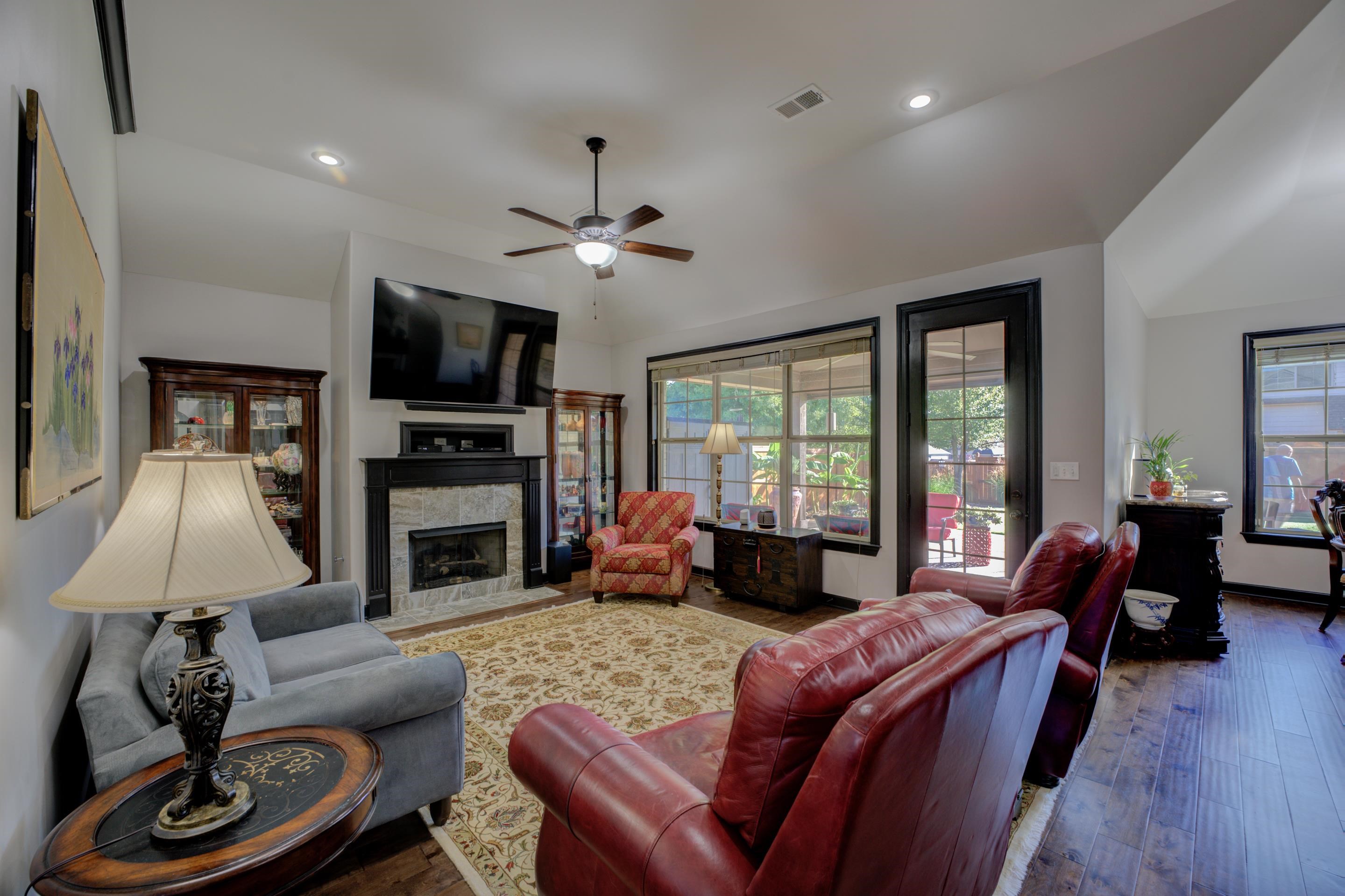 Living room featuring ceiling fan, a tiled fireplace, vaulted ceiling, and dark hardwood / wood-style floors