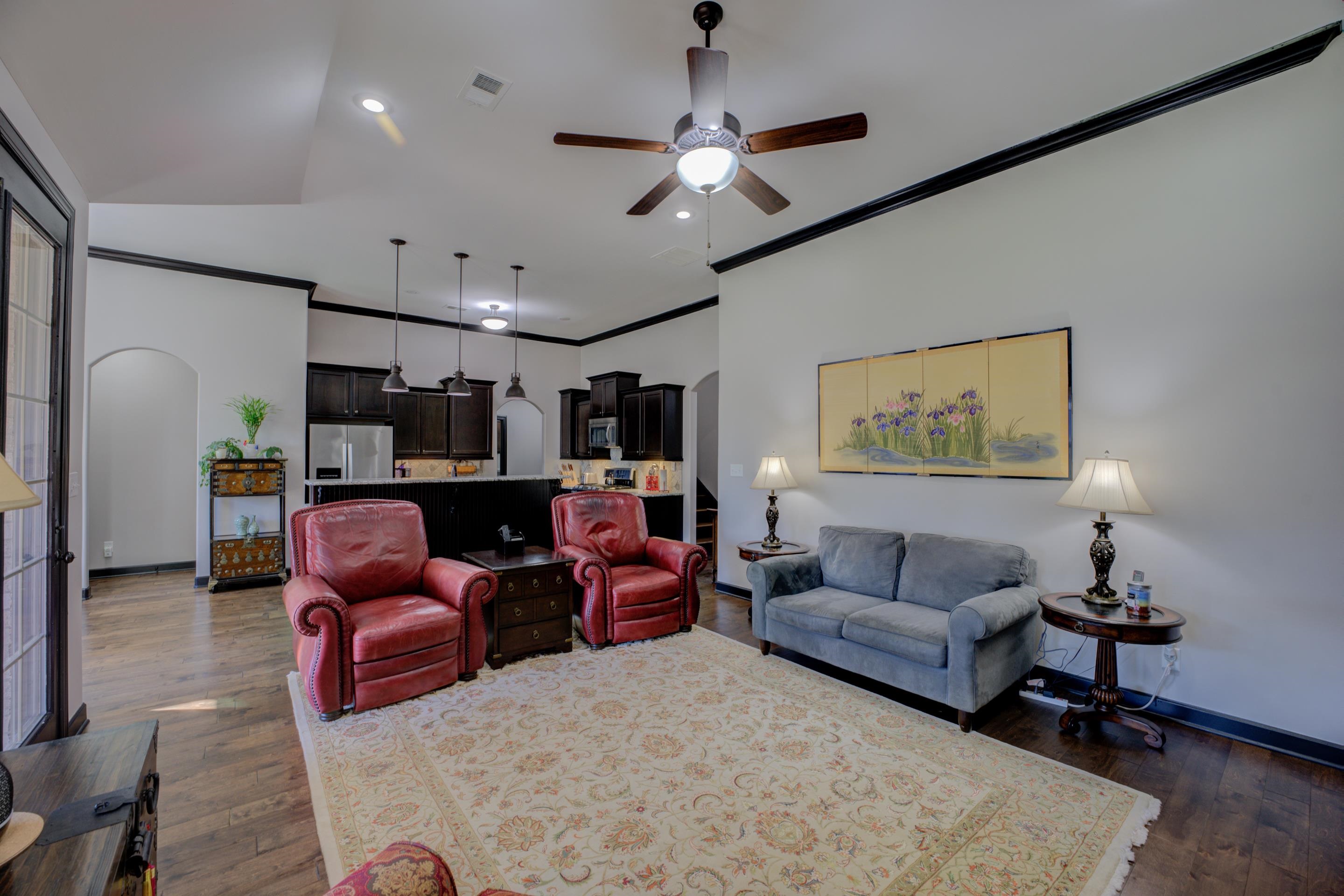 Living room with dark wood-type flooring, crown molding, lofted ceiling, and ceiling fan