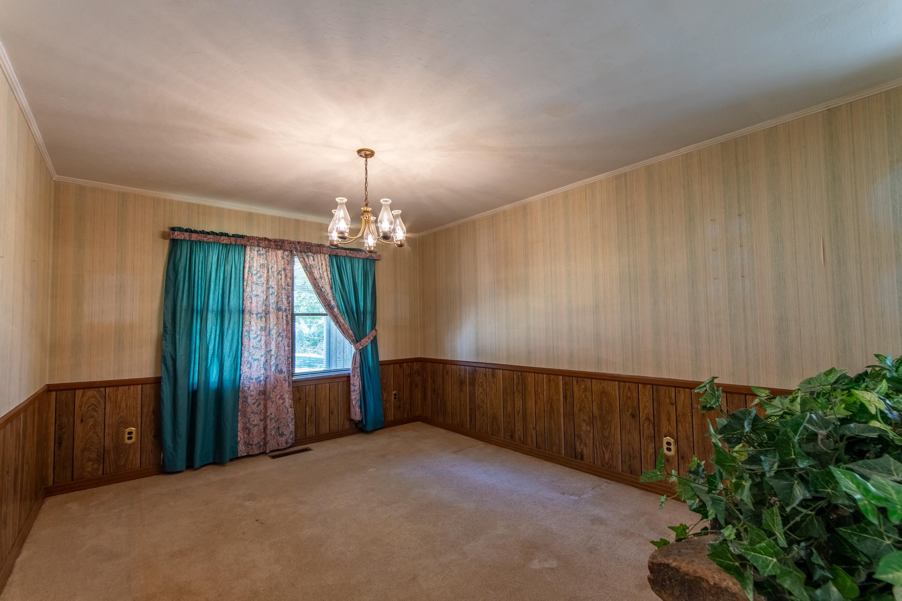 Carpeted spare room with crown molding, a chandelier, and wooden walls