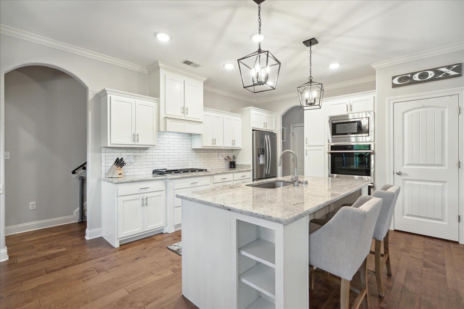 Kitchen with wood-type flooring, sink, an island with sink, white cabinets, and appliances with stainless steel finishes