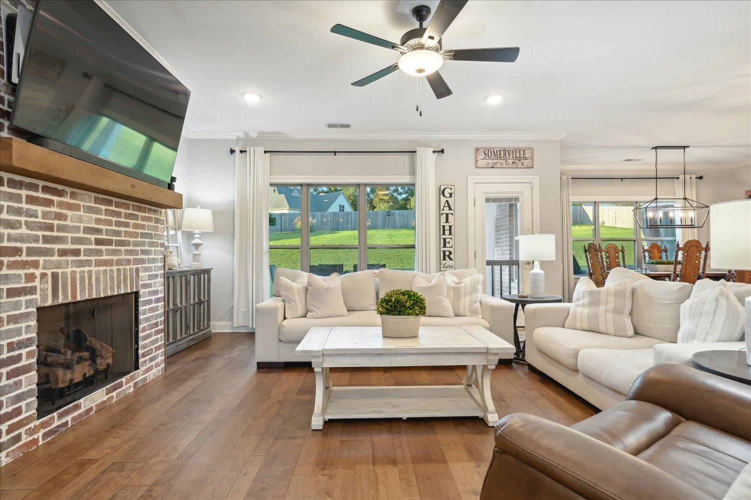 Living room featuring ornamental molding, hardwood / wood-style flooring, a brick fireplace, and ceiling fan with notable chandelier