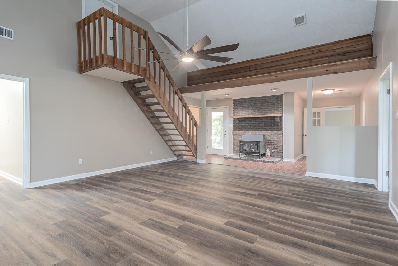 Unfurnished living room featuring a wood stove, high vaulted ceiling, ceiling fan, and wood-type flooring